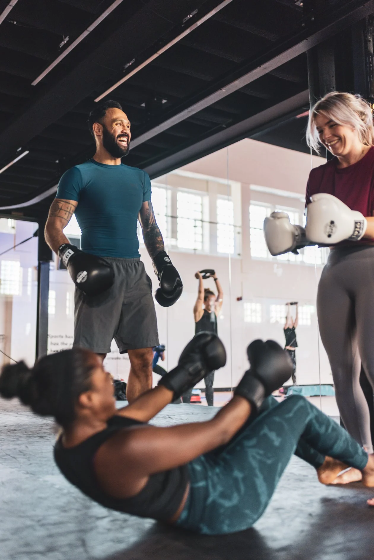 Vrouwen die op de grond liggen en bokshandschoenen dragen tijdens een boxles, terwijl een man met bokshandschoenen lacht en een vrouw met boxing gloves lacht in de sportschool.