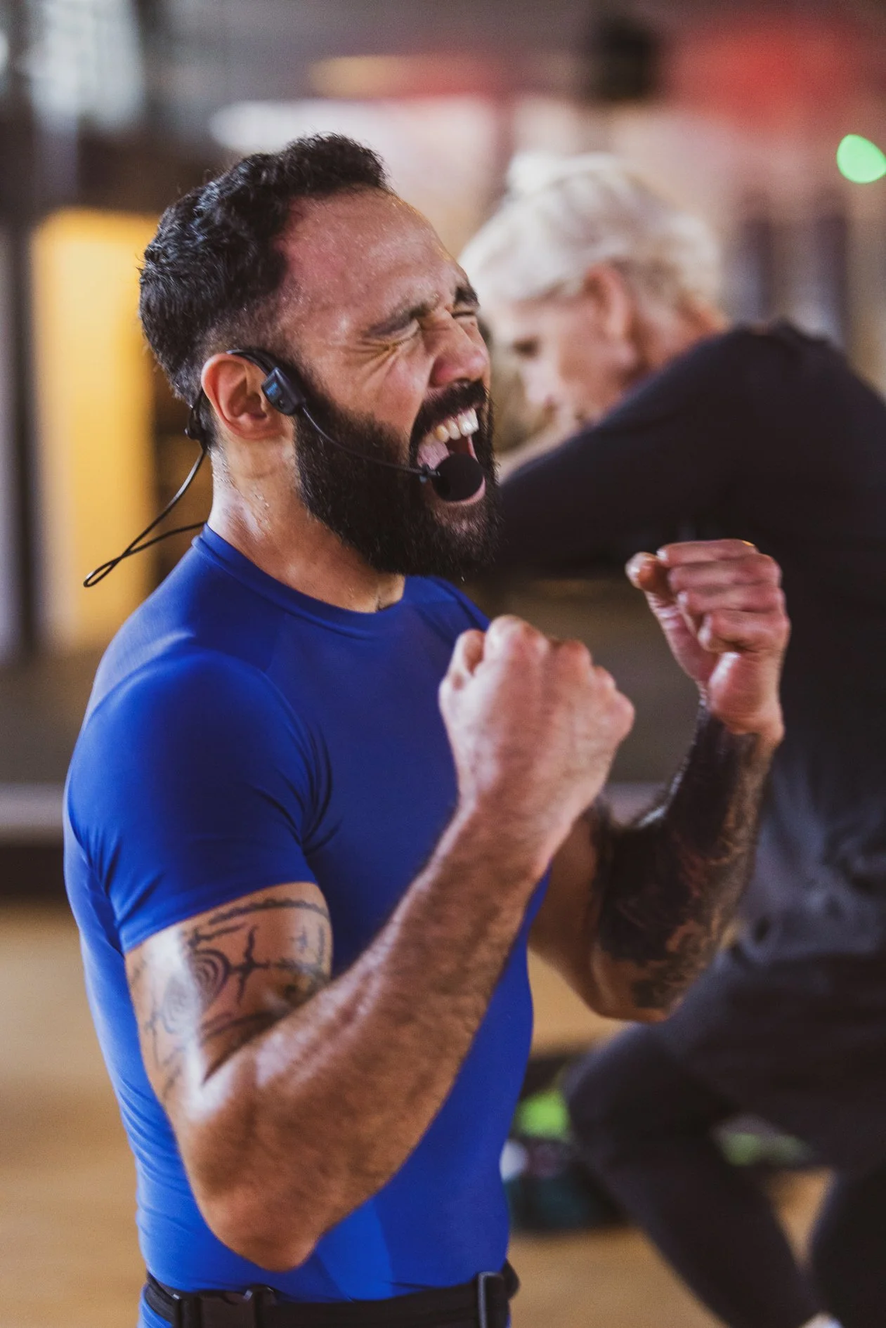 Man met een headset die enthousiast viert, met arm- en fist-handsymbolen, in een sportschool of trainingsruimte.