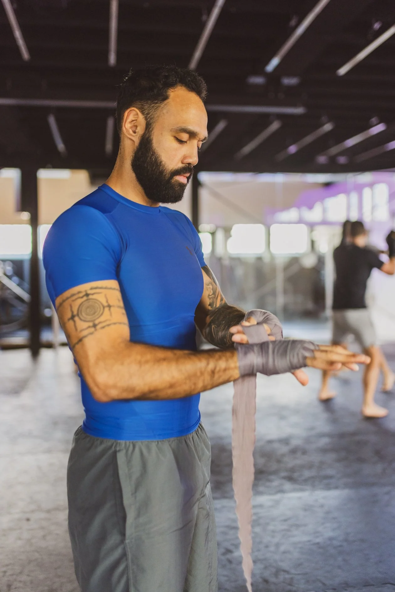 Man in een sportschool die zijn handen inwrapt voor een training, met andere sportschoolbezoekers op de achtergrond.