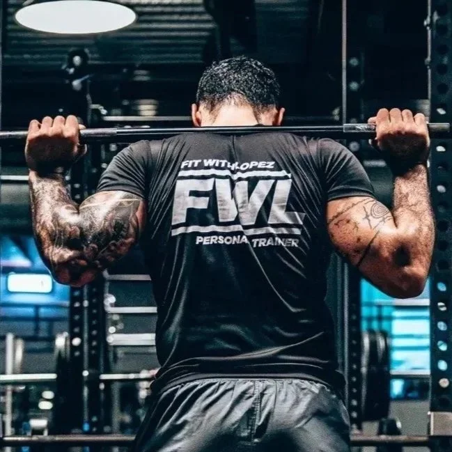 Man tiltet een barbell tijdens krachttraining in een fitnessruimte, met zicht op spiergetrainde armen en rug.