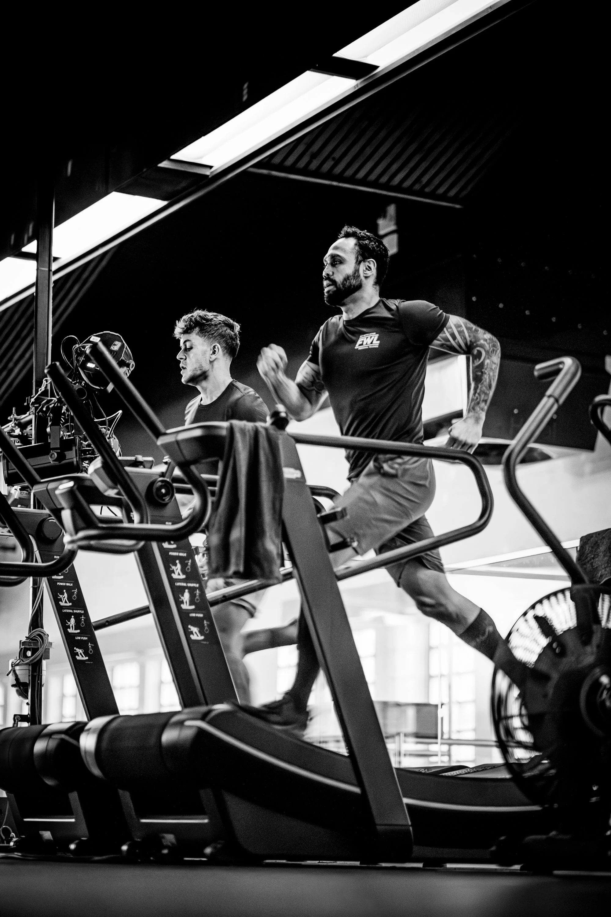 Two men running on treadmills in a gym, black and white photo.