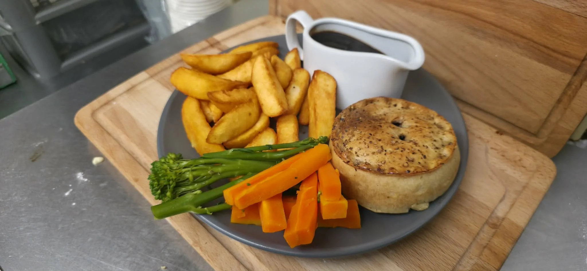 Plate with potato wedges, steamed vegetables, beef Wellington, and a small pitcher of gravy.