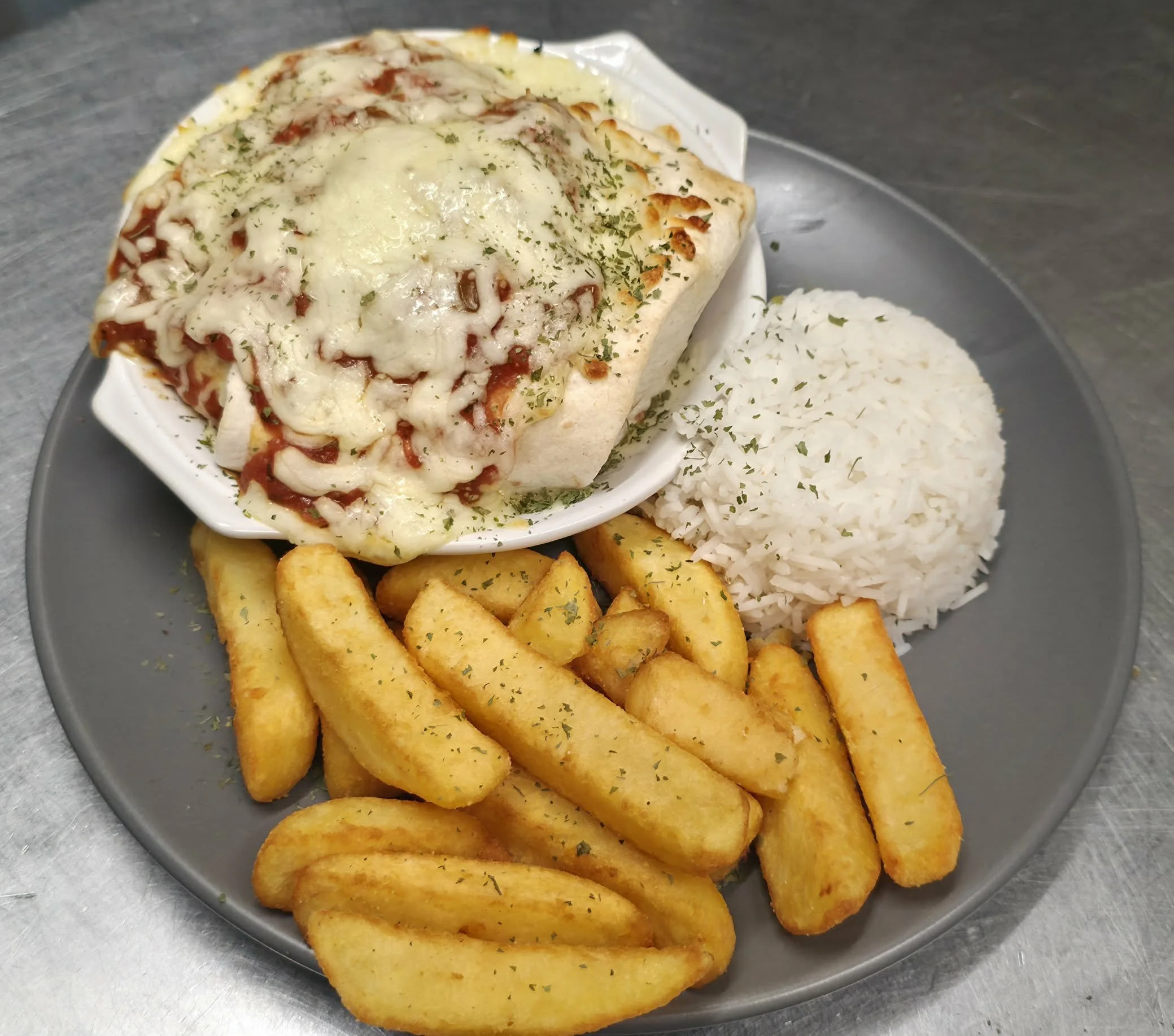Plate of cheesy baked casserole, white rice, and seasoned potato fries garnished with parsley.