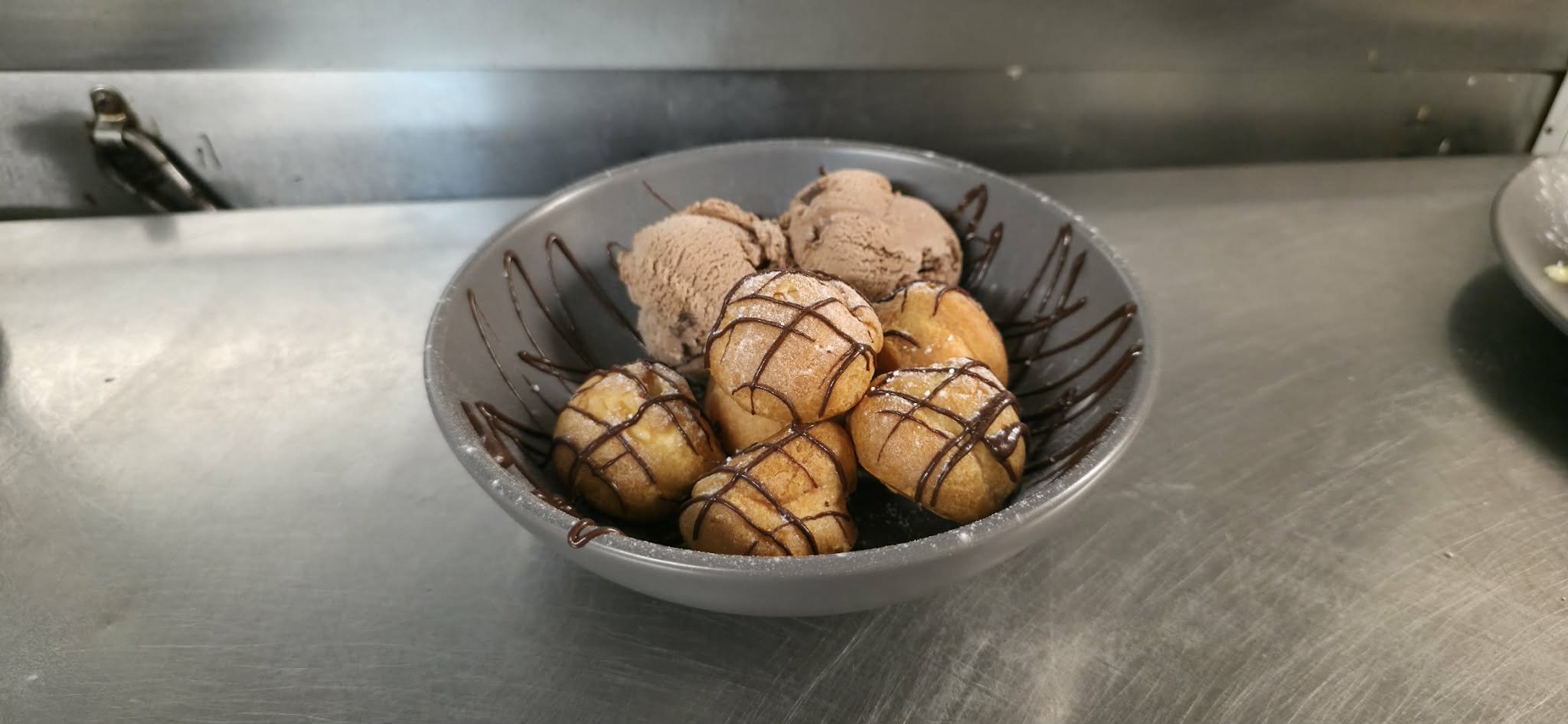A bowl of fried dough balls topped with chocolate drizzle and served with scoops of chocolate ice cream.