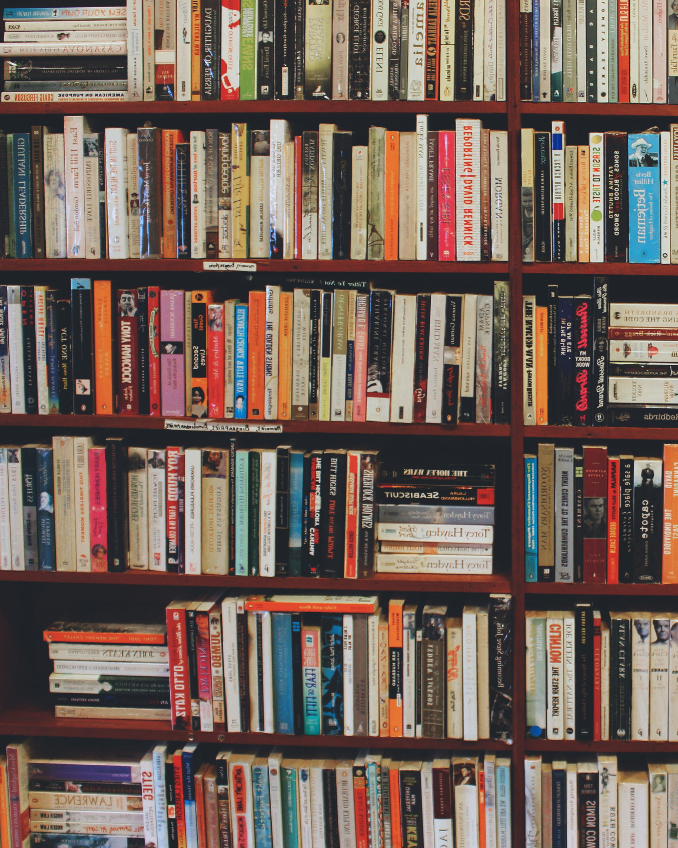 Books of various sizes and colors arranged vertically and horizontally on a wooden bookshelf.