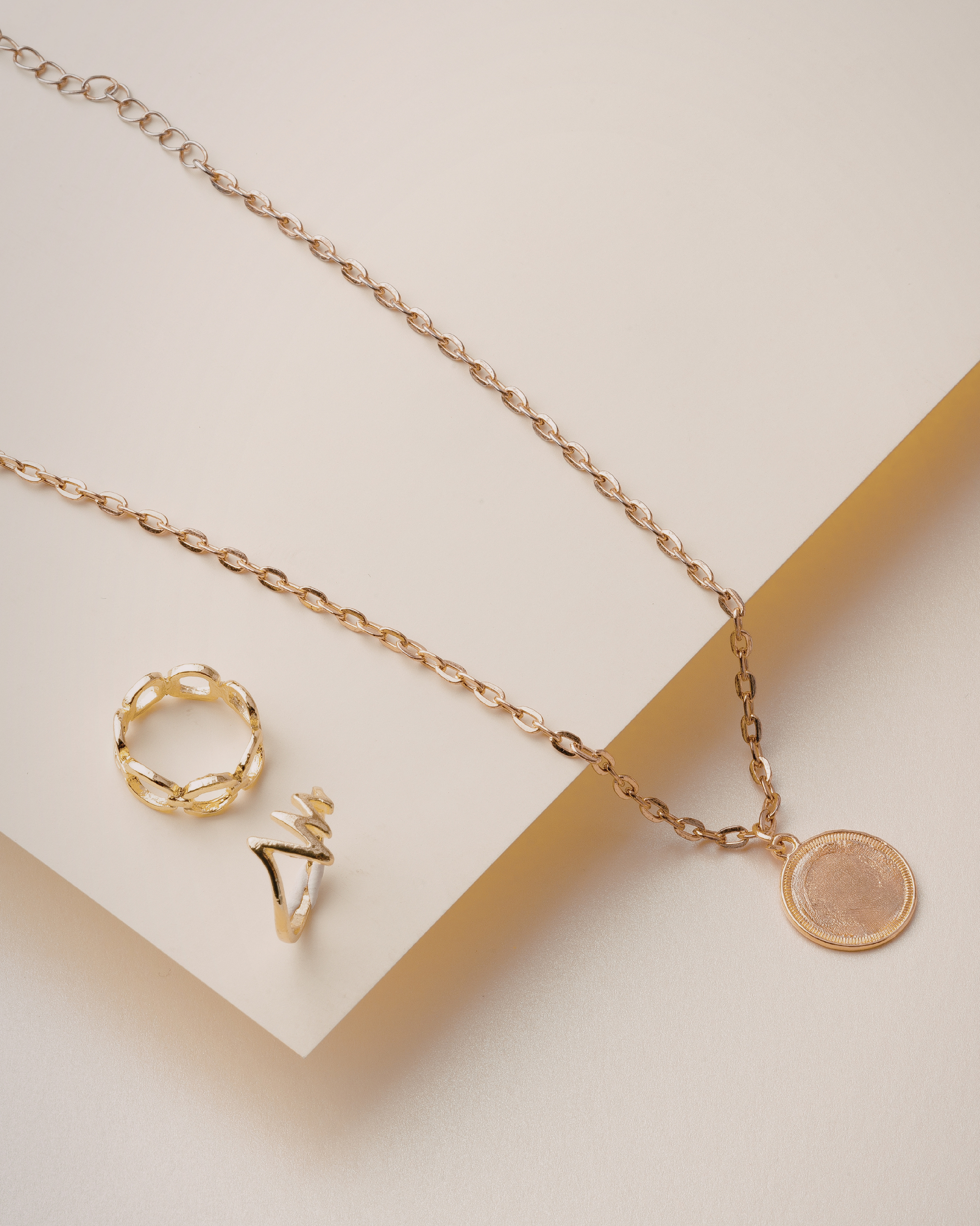 Columbus hidden gems showing a gold chain necklace with a round pendant, a textured gold ring, and a sculptural gold ring on a beige surface.