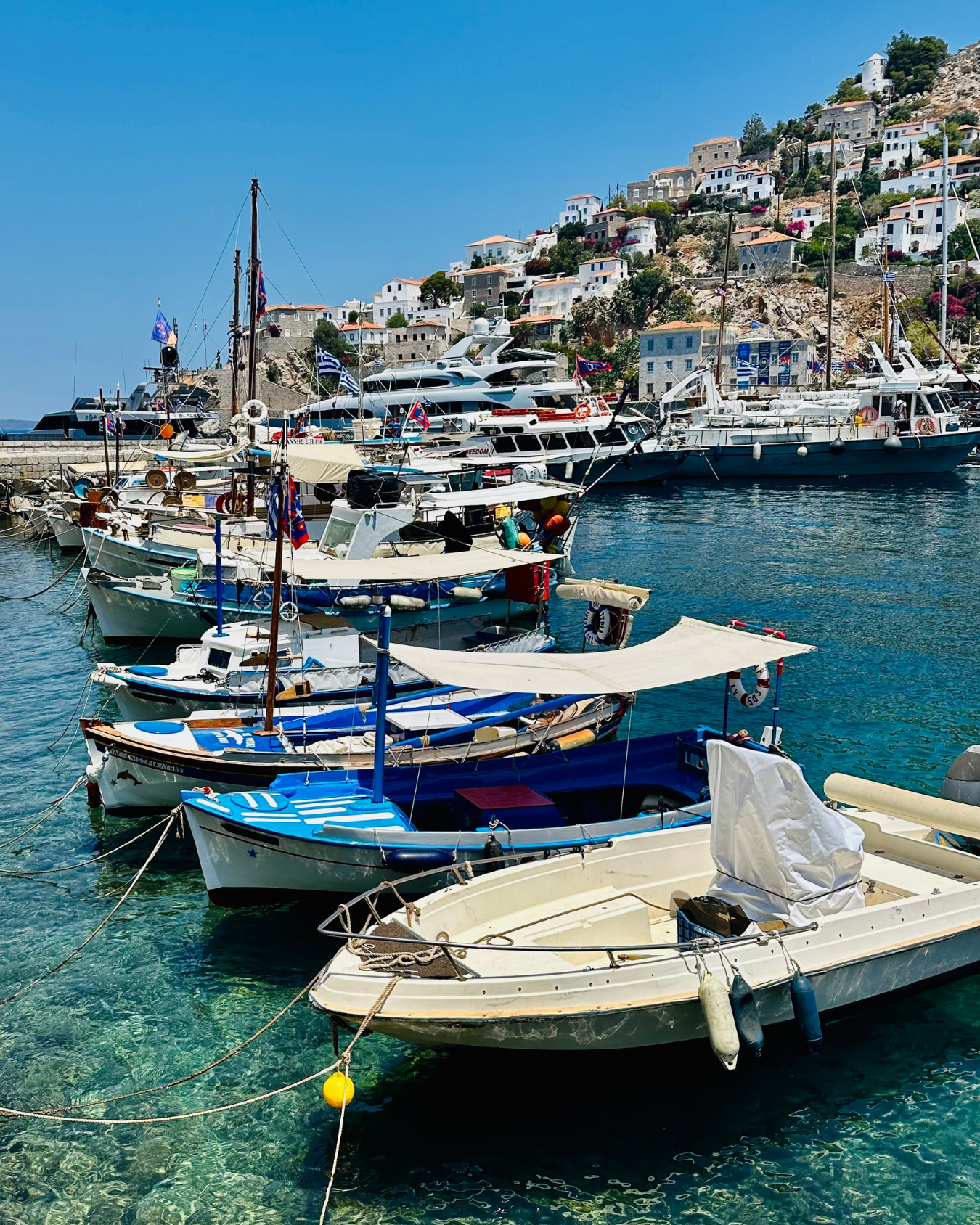 Real estate agent who helps with downsizing in Columbus and travels to places with small boats and yachts docked in a clear blue harbor with white hillside buildings in the background.