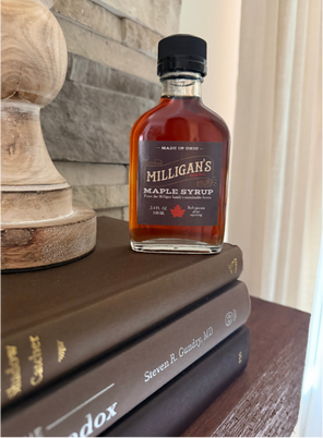 Amanda Lucy, Columbus Ohio Realtor gifts a small bottle of Milligan's Maple Syrup sits on top of a stack of books next to a wooden object.