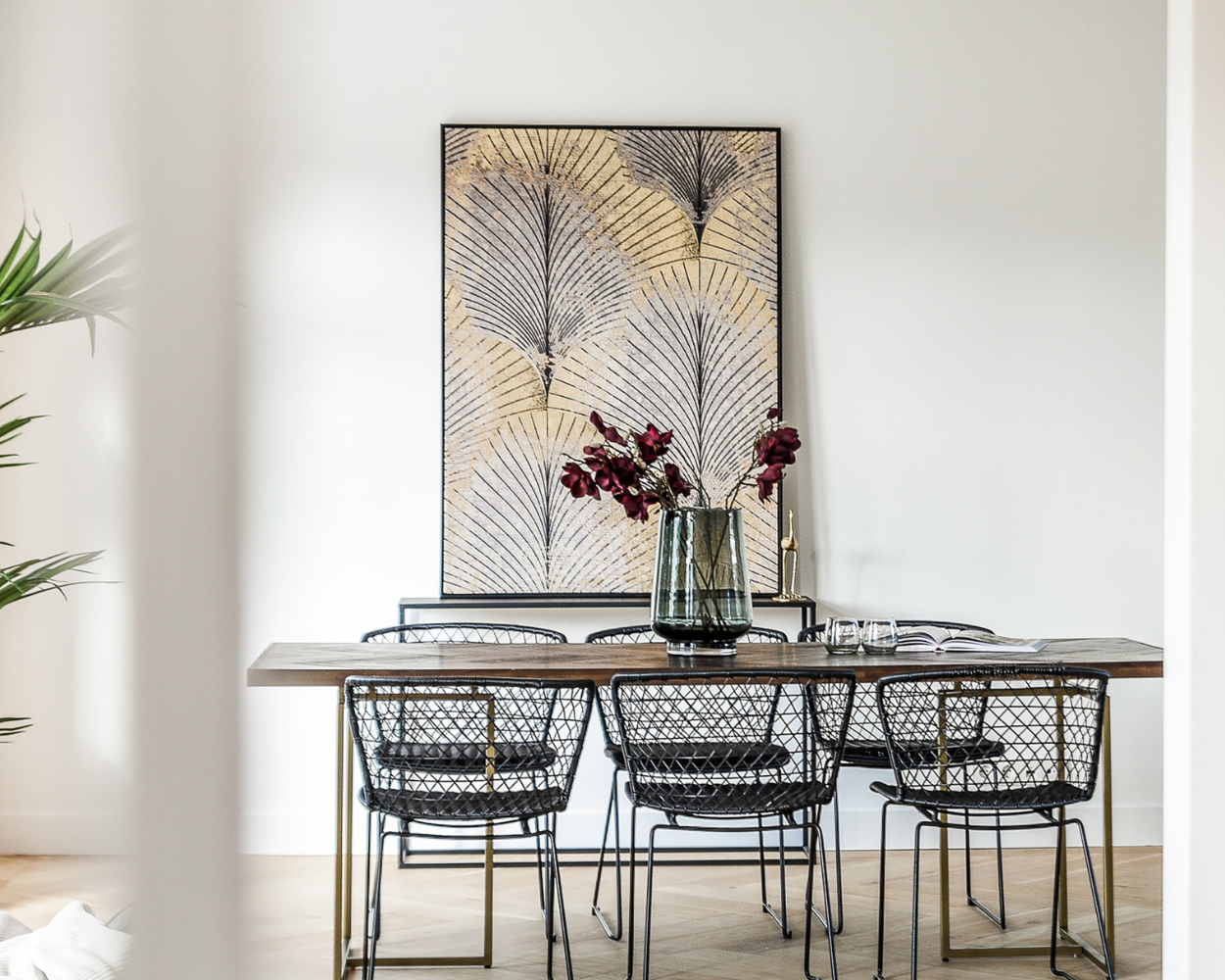 Best Real Estate Agent in Columbus Ohio for a modern dining room with a rectangular table, six wire chairs, a vase with flowers, and abstract leaf wall art.