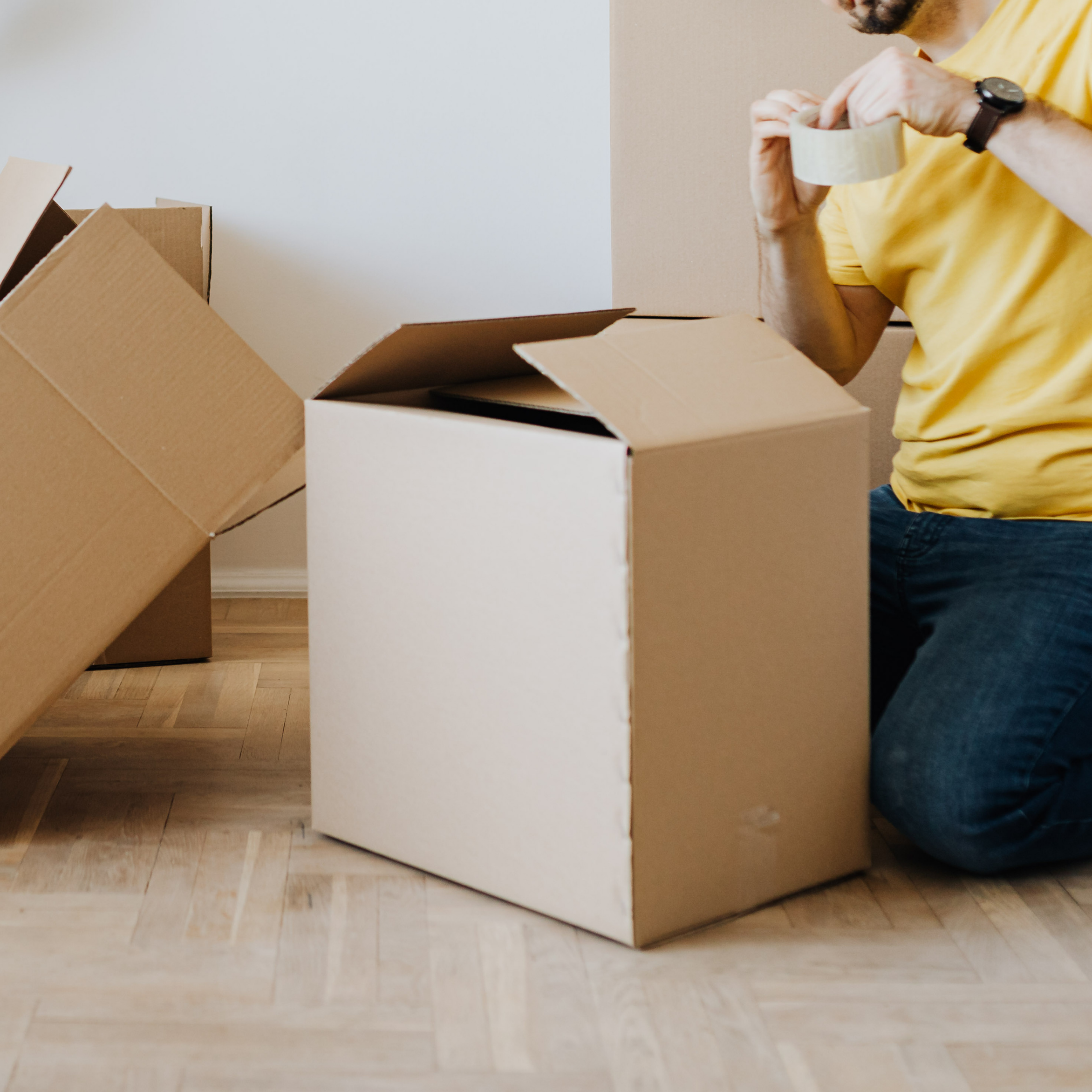 Amanda Lucy's kid's helped sealing a cardboard box with packing tape while a client was moving, surrounded by other open boxes on a wooden floor.