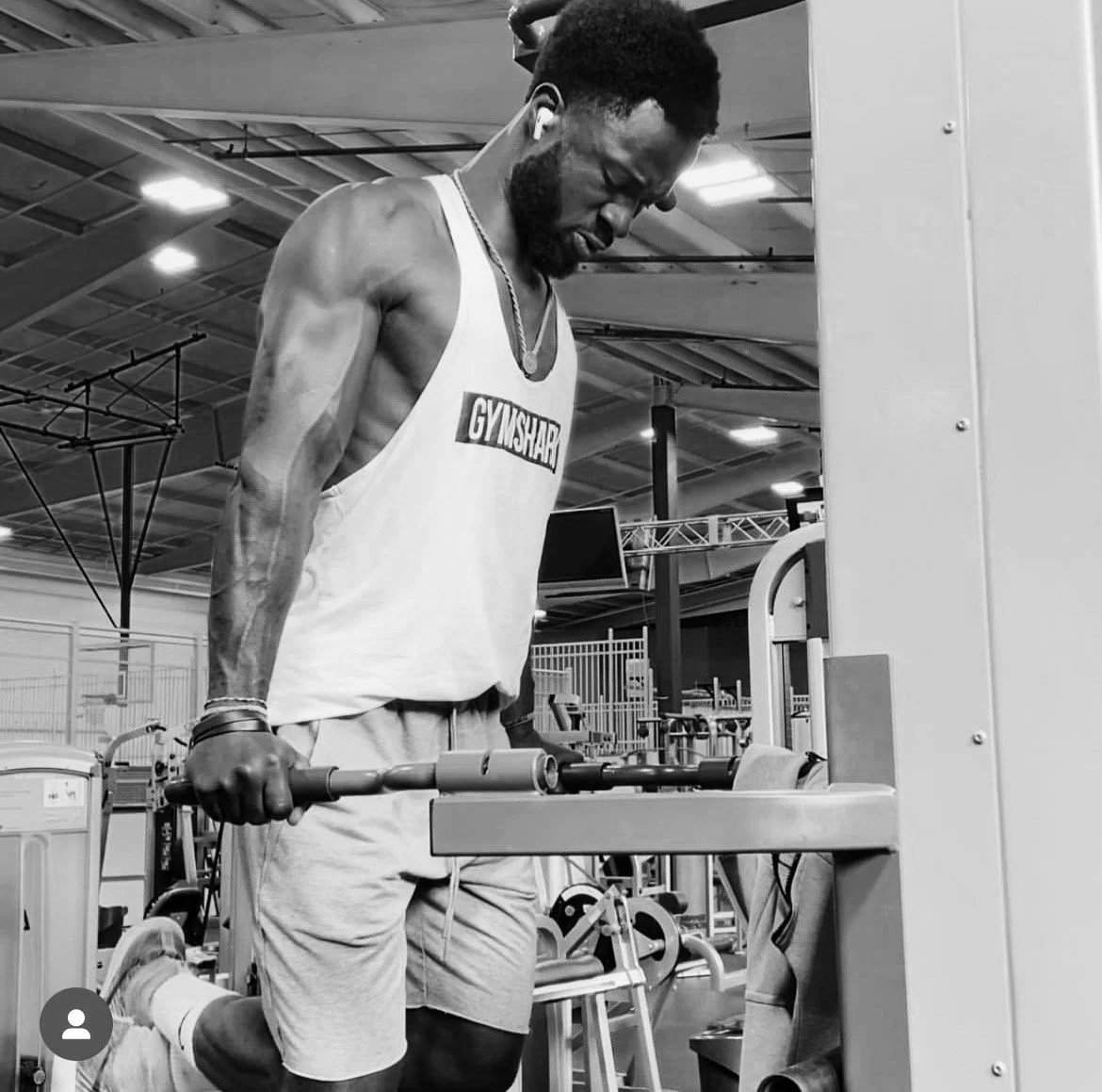 A man with a beard and athletic build exercises with weights at the gym, wearing a tank top that says 'GYMSHARK'.