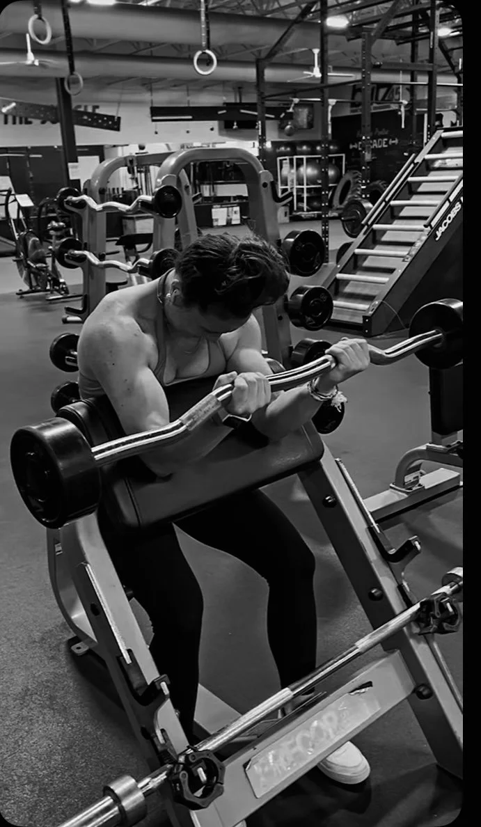 Woman working out with a barbell on a preacher curl bench in a gym.