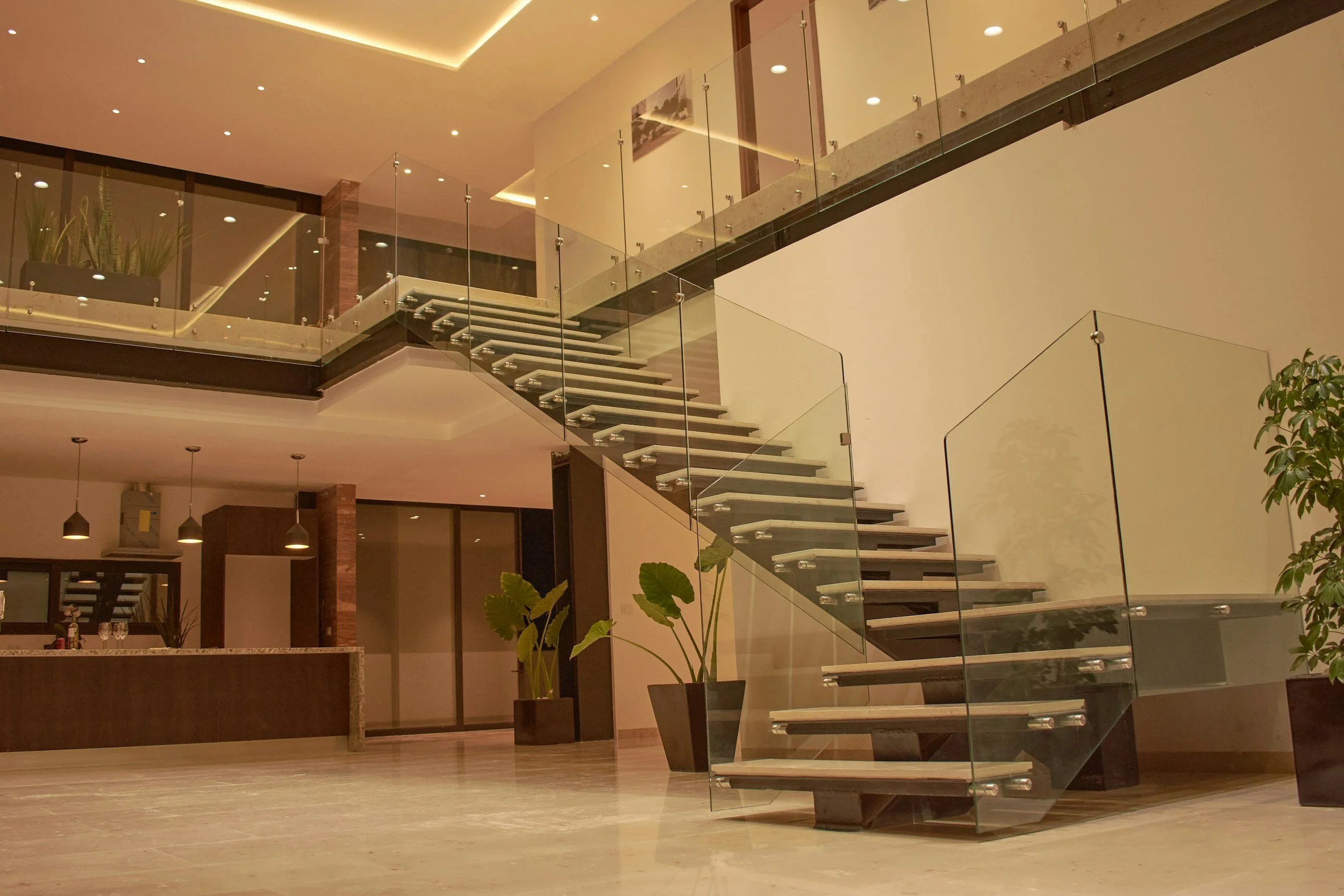 Interior of a modern building with a glass staircase, potted plants, and a reception desk.