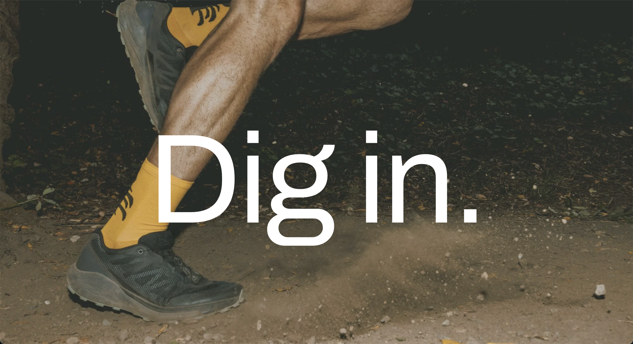 Close-up of a person's legs and feet running on a dirt trail, wearing black running shoes, yellow socks, and yellow shorts, with the word 'Dig in.' overlaid.