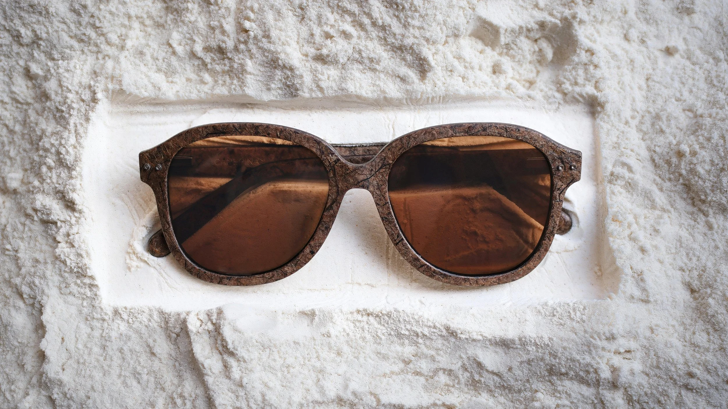 Brown sunglasses with a textured frame resting on a white textured surface.