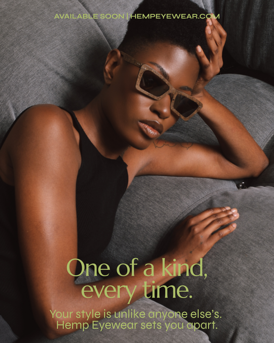 A woman lying on a gray couch, wearing large sunglasses and a black top, with one arm resting on her forehead. She has short hair and a tattoo on her arm. Green text over the image reads: 'AVAILABLE SOON | HEMPYEWEAR.COM'. Below, larger green text says: 'One of a kind, every time.' Smaller green text underneath states: 'Your style is unlike anyone else's. Hemp Eyewear sets you apart.'