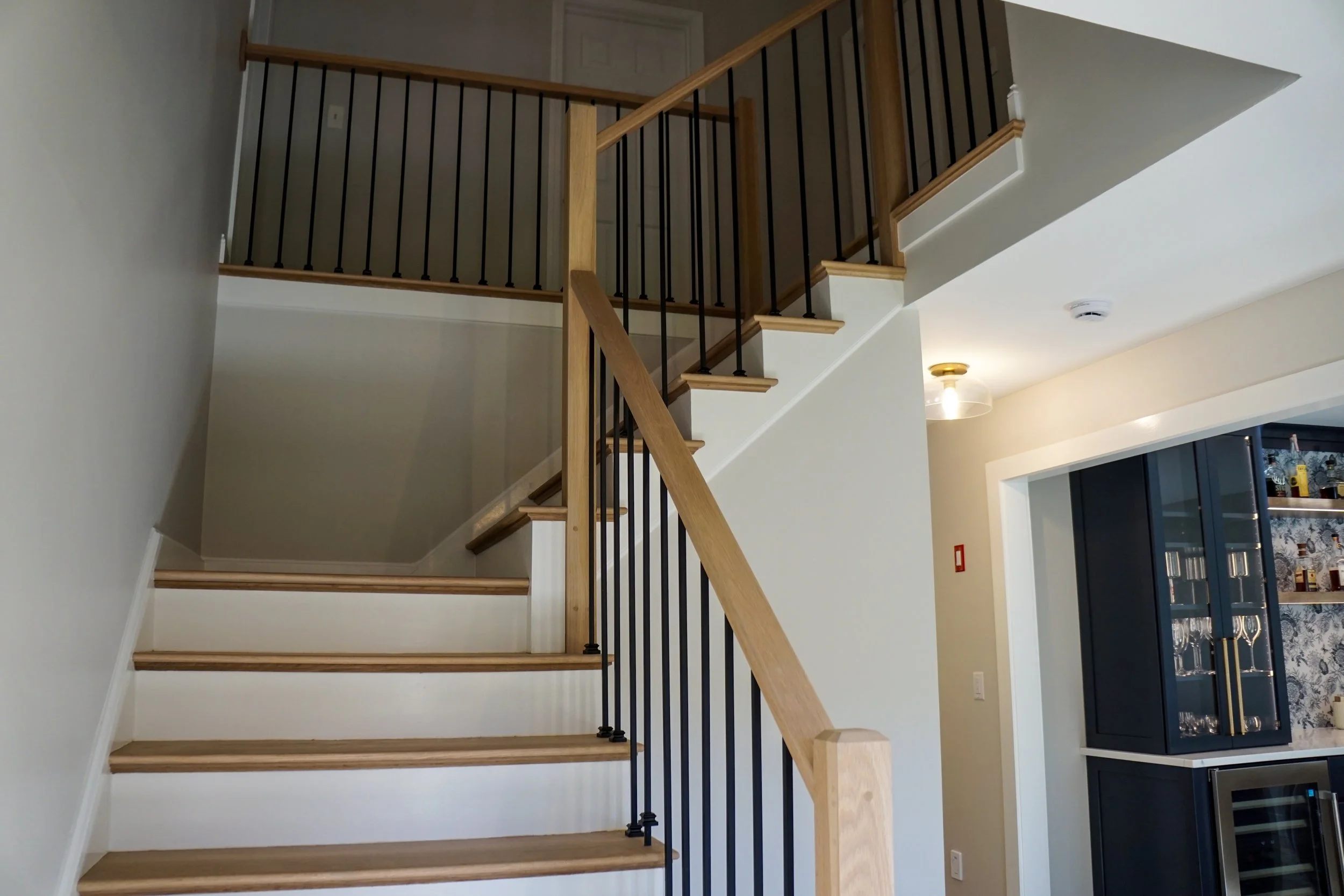 Interior view of a staircase with wooden steps and black metal balusters, leading to an upper floor in a modern home.