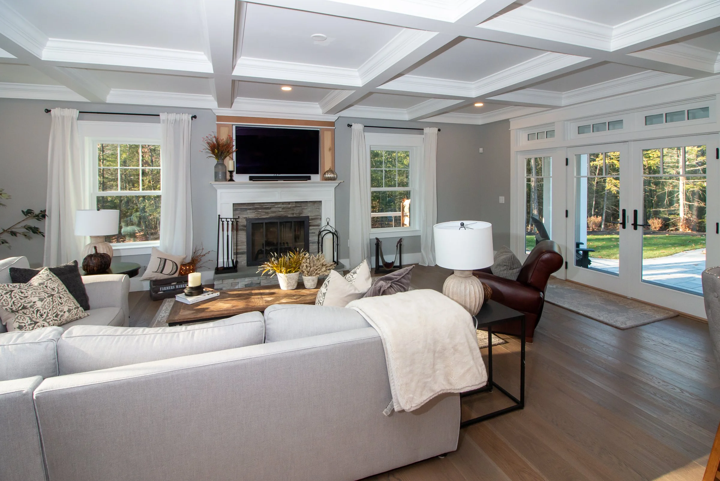 Bright living room with white sofa, wood coffee table, fireplace, large windows, and glass sliding doors leading outside.