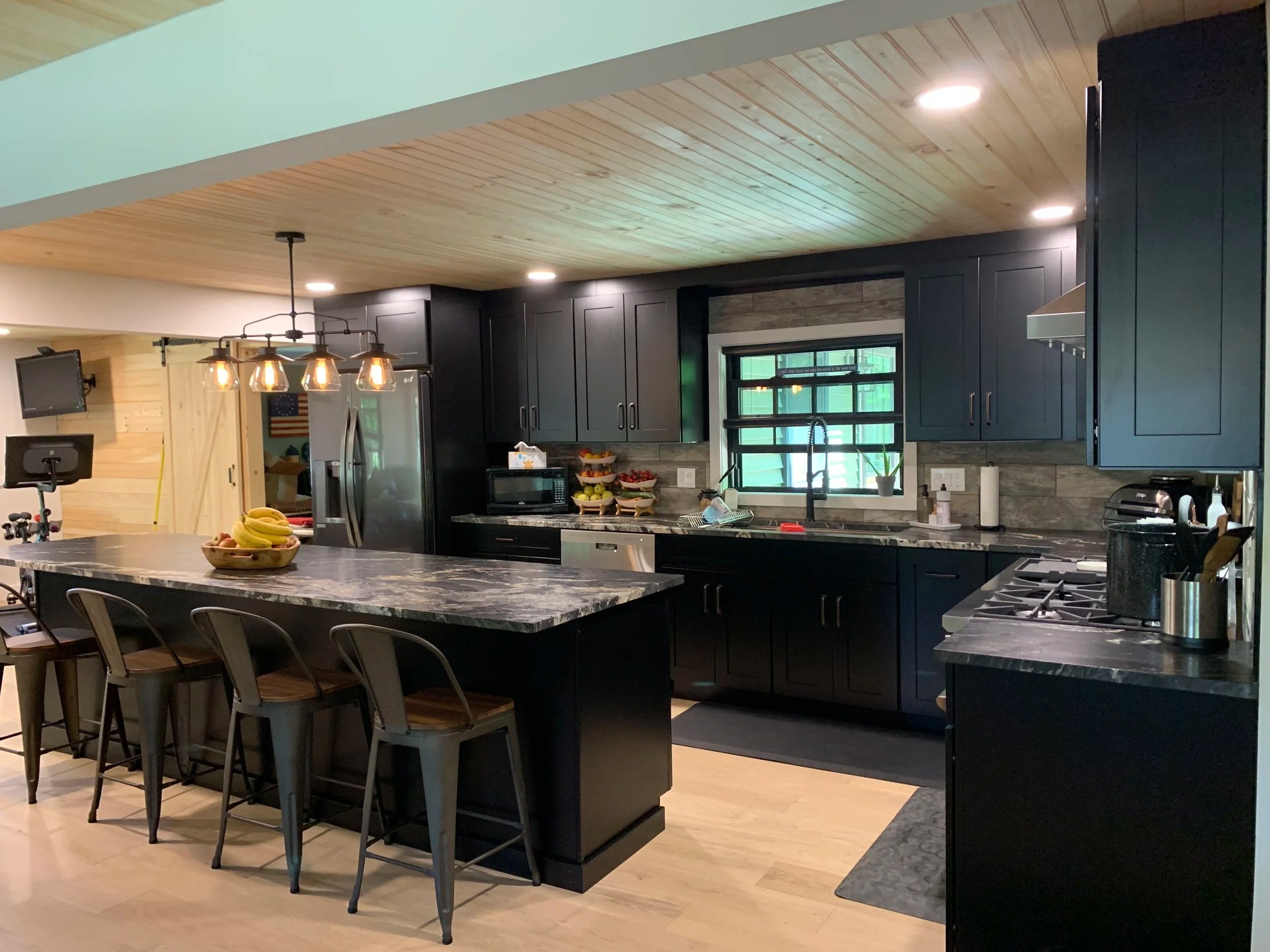Modern kitchen with black cabinets, a large marble island with four chairs, a window above the sink, and various kitchen appliances and decor.