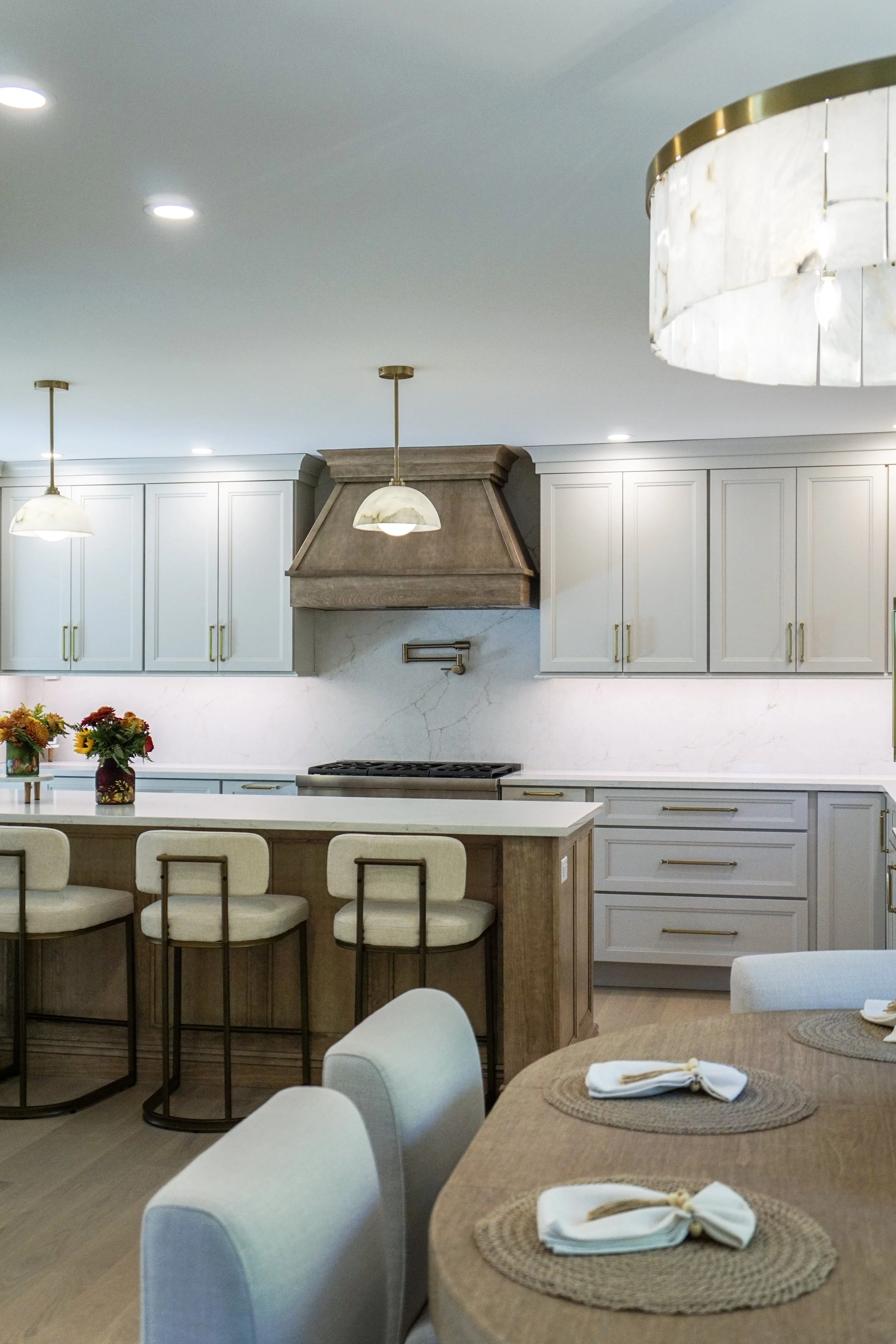 Modern kitchen with white cabinetry, a marble backsplash, a wooden kitchen island with bar stools, and a dining table with placemats and napkins.