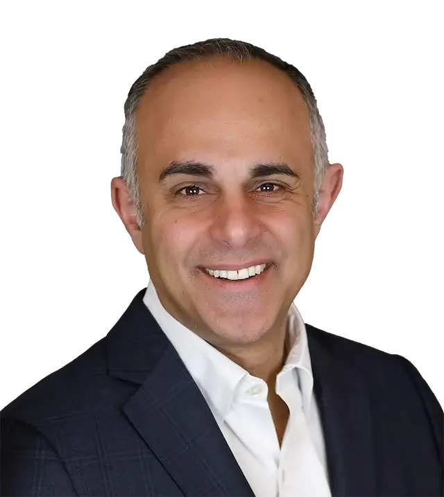 Headshot of a smiling middle-aged man with short gray hair, wearing a dark suit and white shirt, against a dark background.