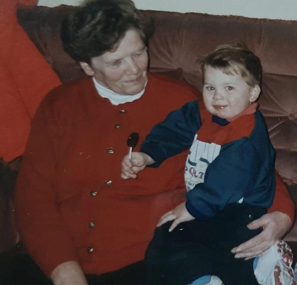 An elderly woman sitting on a couch with a young boy on her lap, holding a black lollipop.