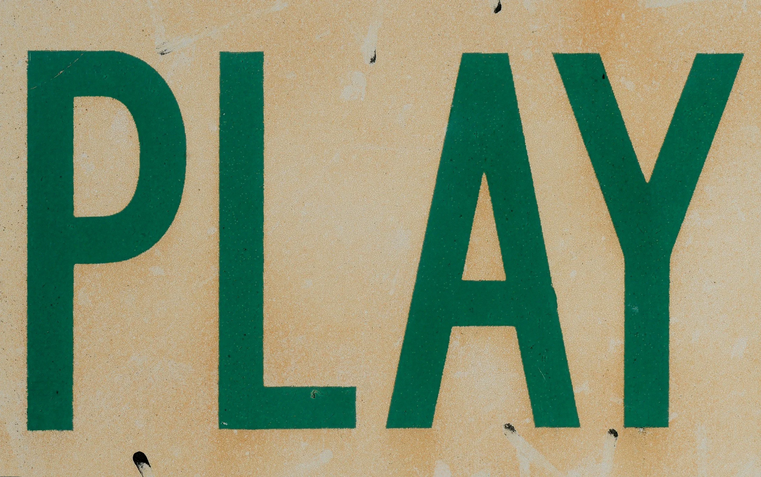 Close-up of a sign with the word 'PLAY' in large green capital letters on a beige background.