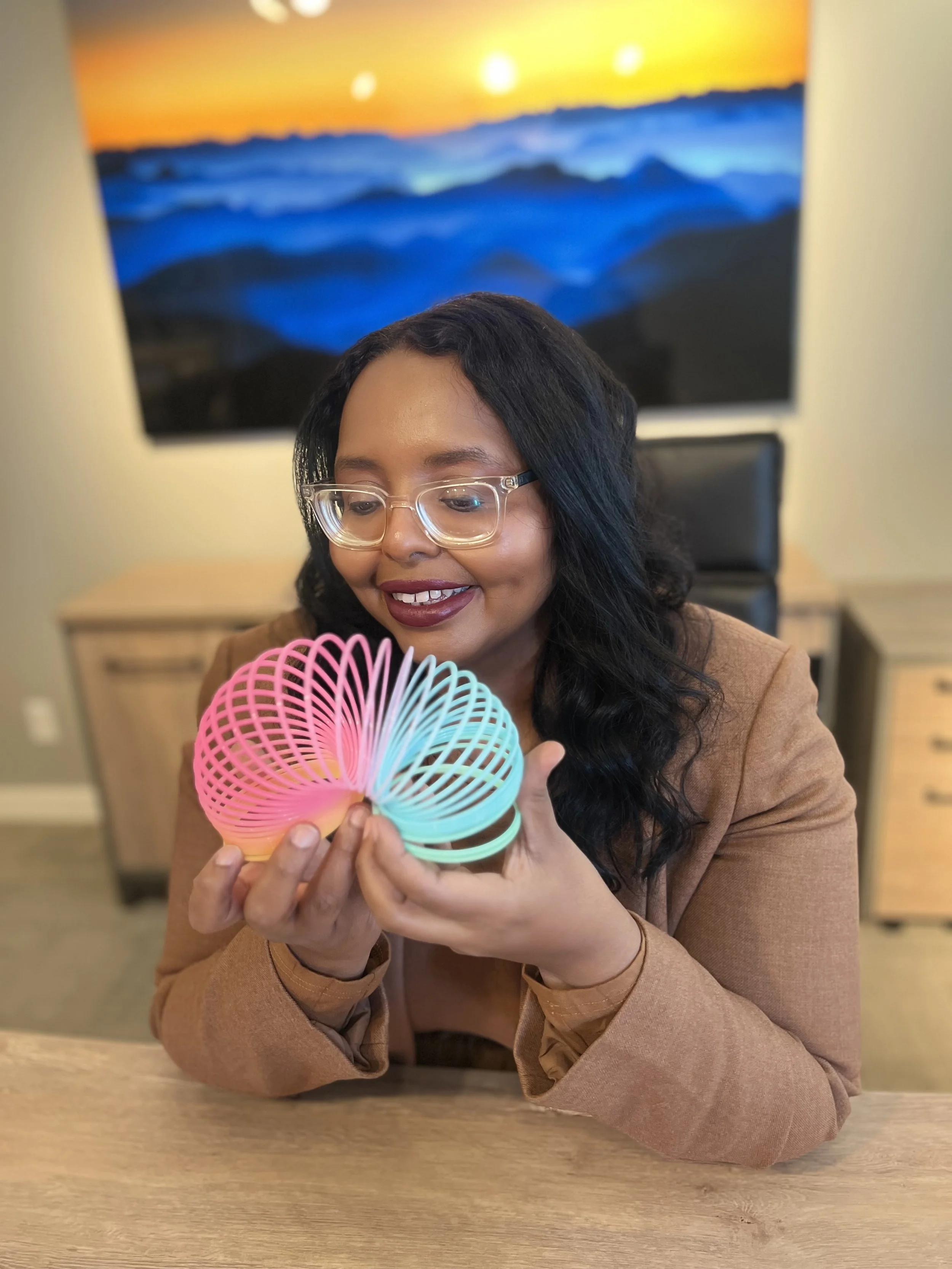 Woman with glasses smiling while holding a colorful spiky toy in an office.