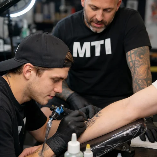Tattoo student performing a supervised tattoo on a real client in a professional studio setting