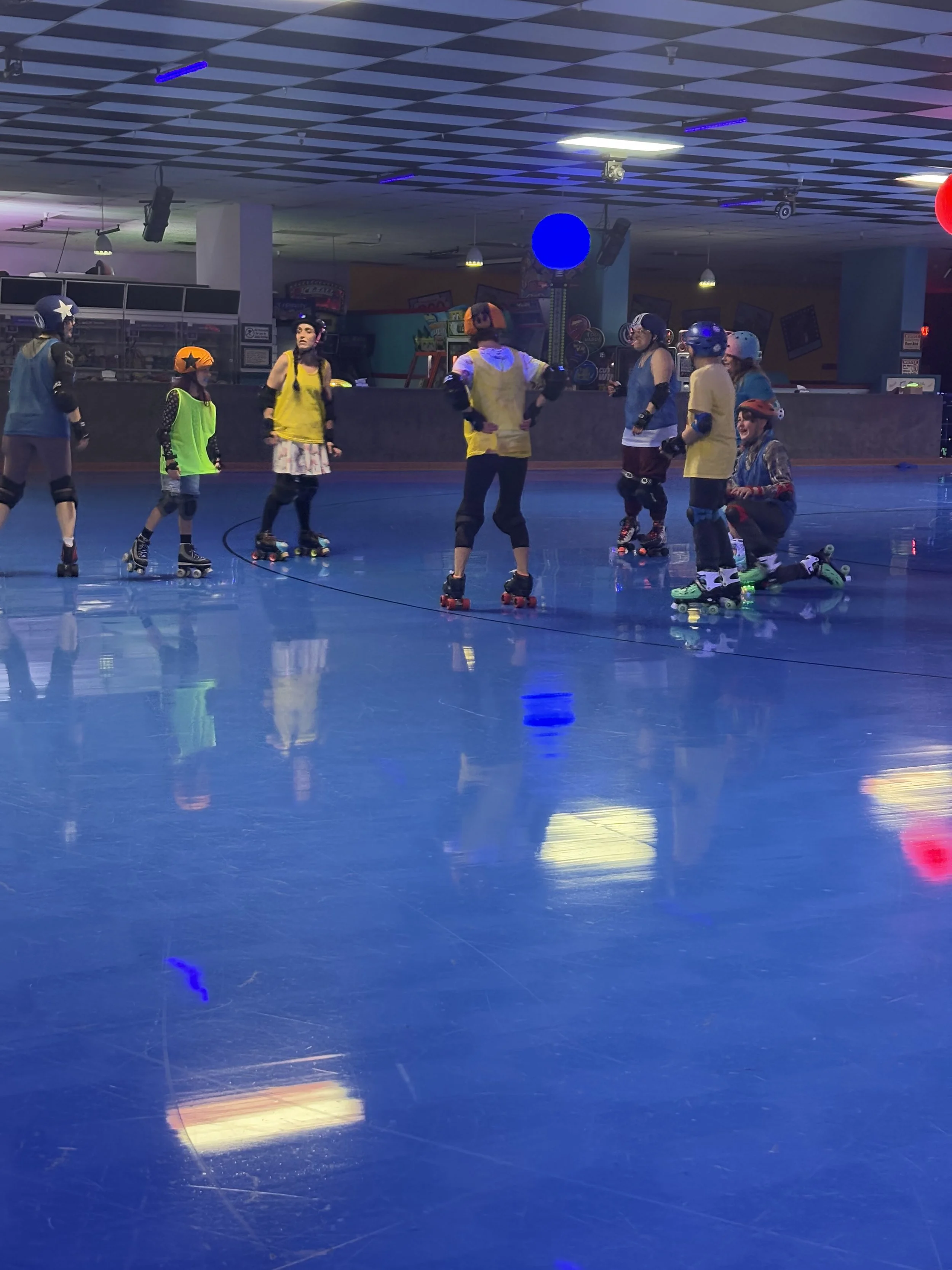 Children roller skating inside an indoor roller rink with a shiny blue floor and colorful lighting.