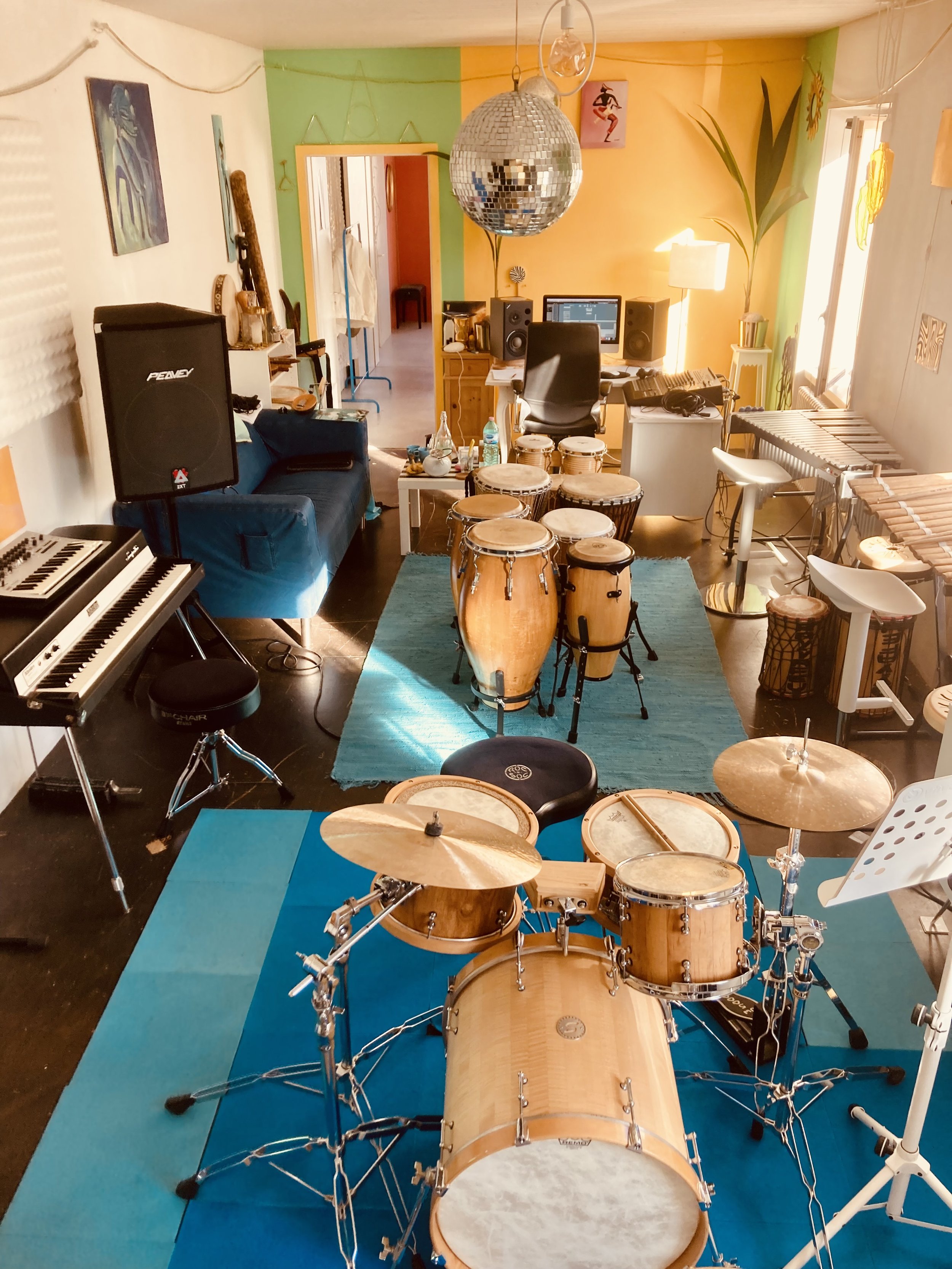 Musikzimmer mit Schlagzeug, Keyboard, Computer, Lautsprecher, Gitarren, Mücken, Möbel und Dekorationen in bunten Farben.