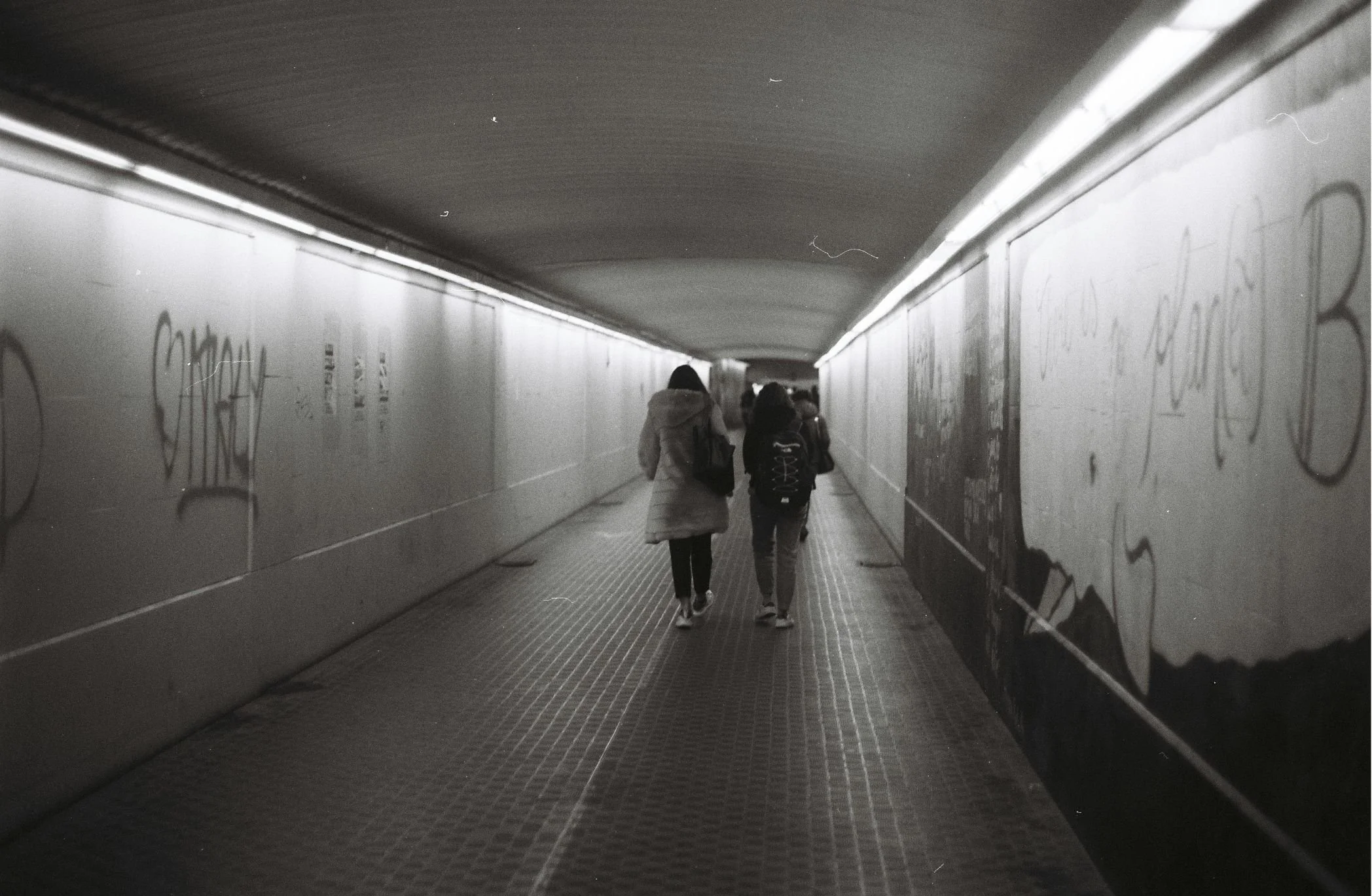 People walking through an underground pedestrian tunnel with graffiti on the walls.