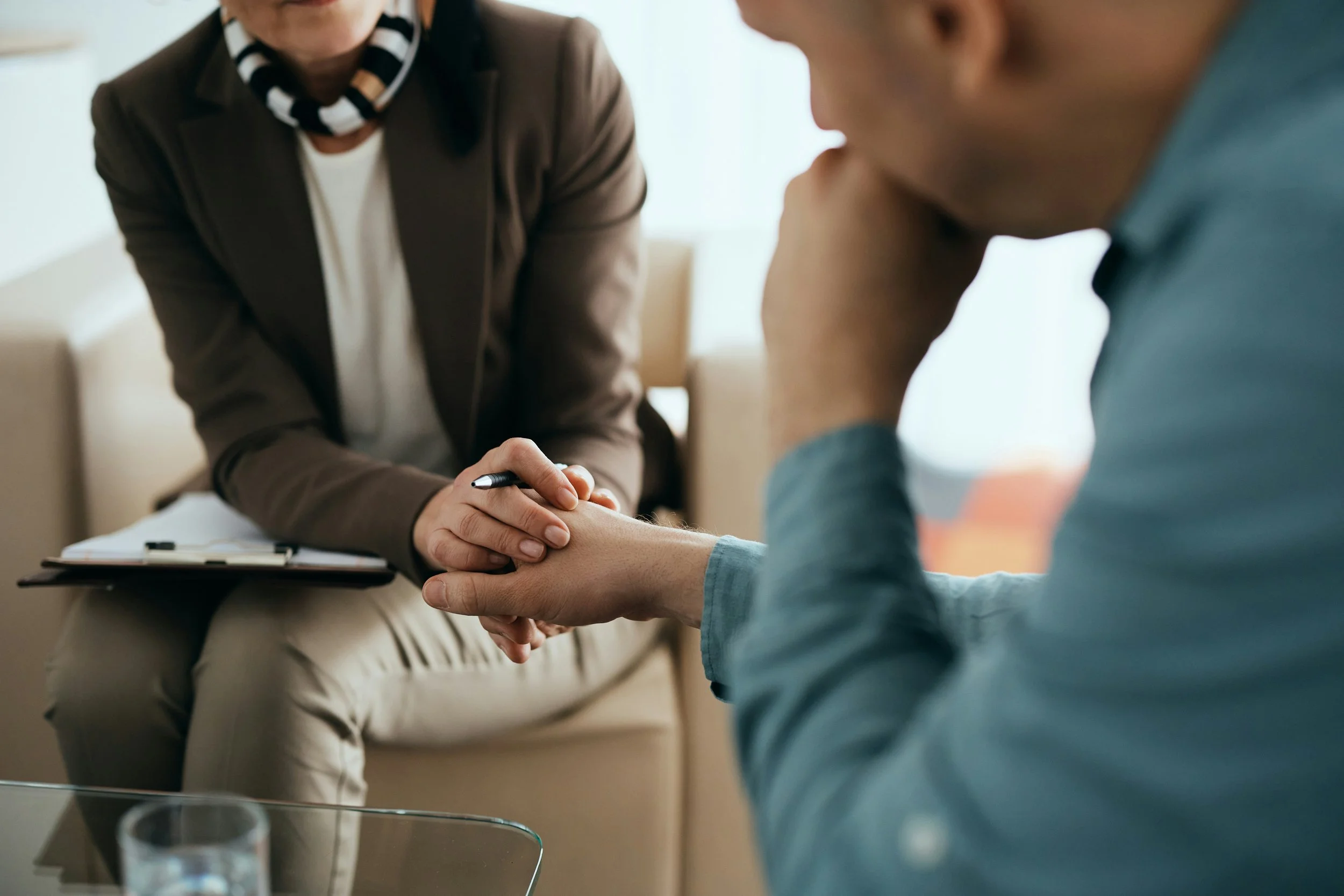 A man and a woman holding hands during a counseling session in a therapist's office.