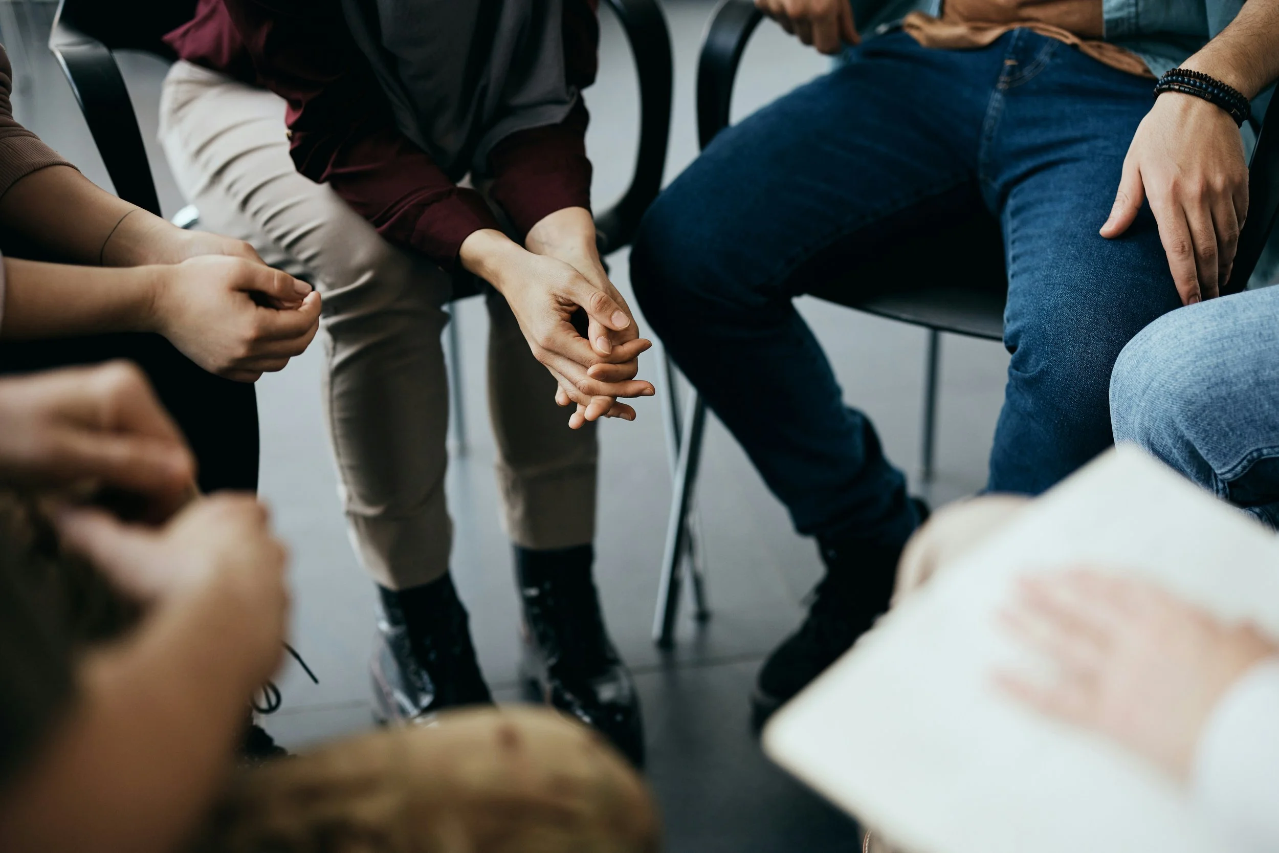 A group of people sitting in a circle, holding hands during a support group or meeting.