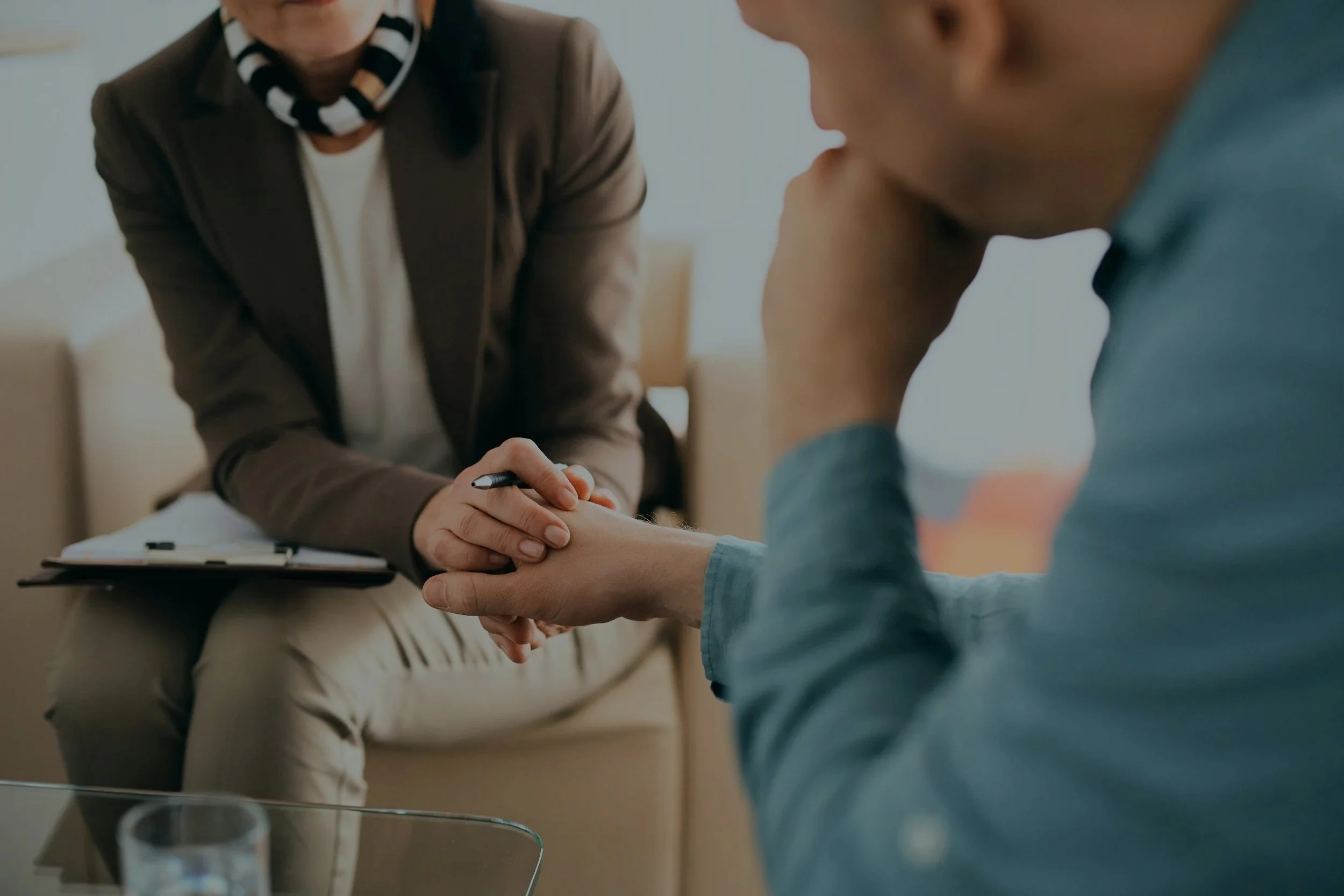 A woman counselor sitting on a couch holding a client's hand during a counseling session, with both appearing engaged and empathetic.