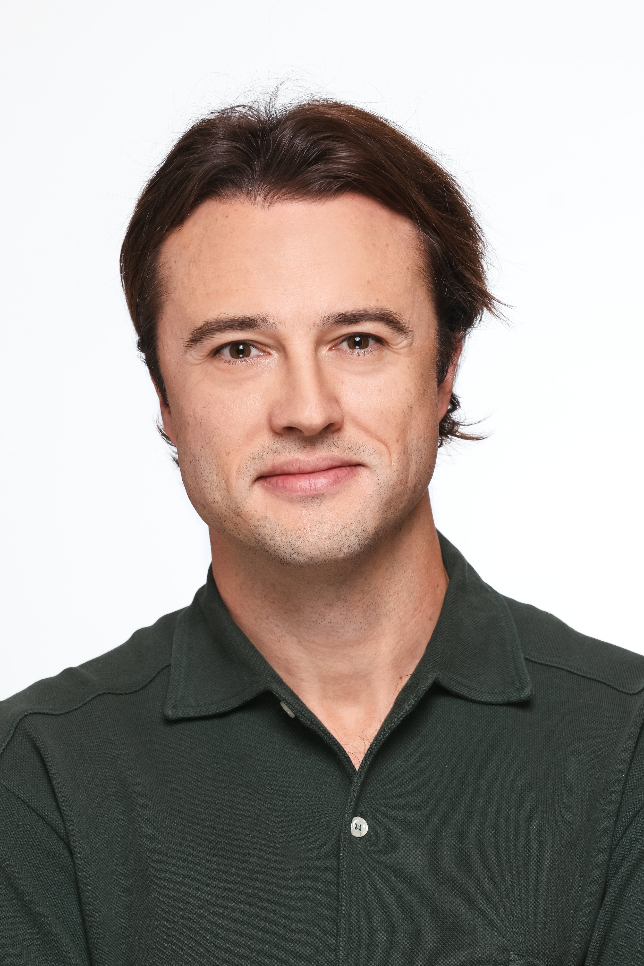 Close-up portrait of a man with brown hair and blue eyes, wearing a dark green collared shirt, against a white background.