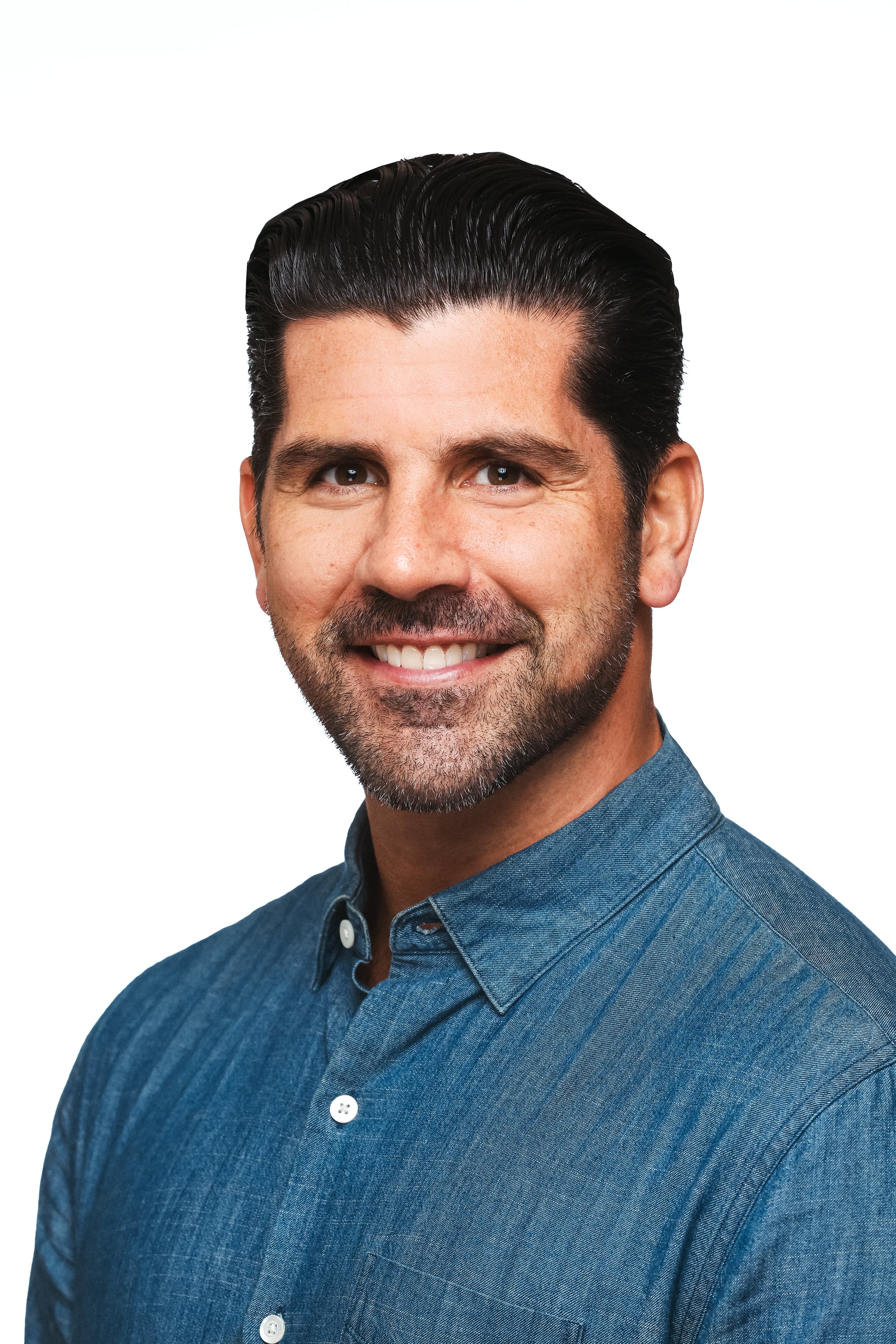 Headshot of a smiling man with dark hair, a beard, wearing a blue button-up shirt, against a white background.