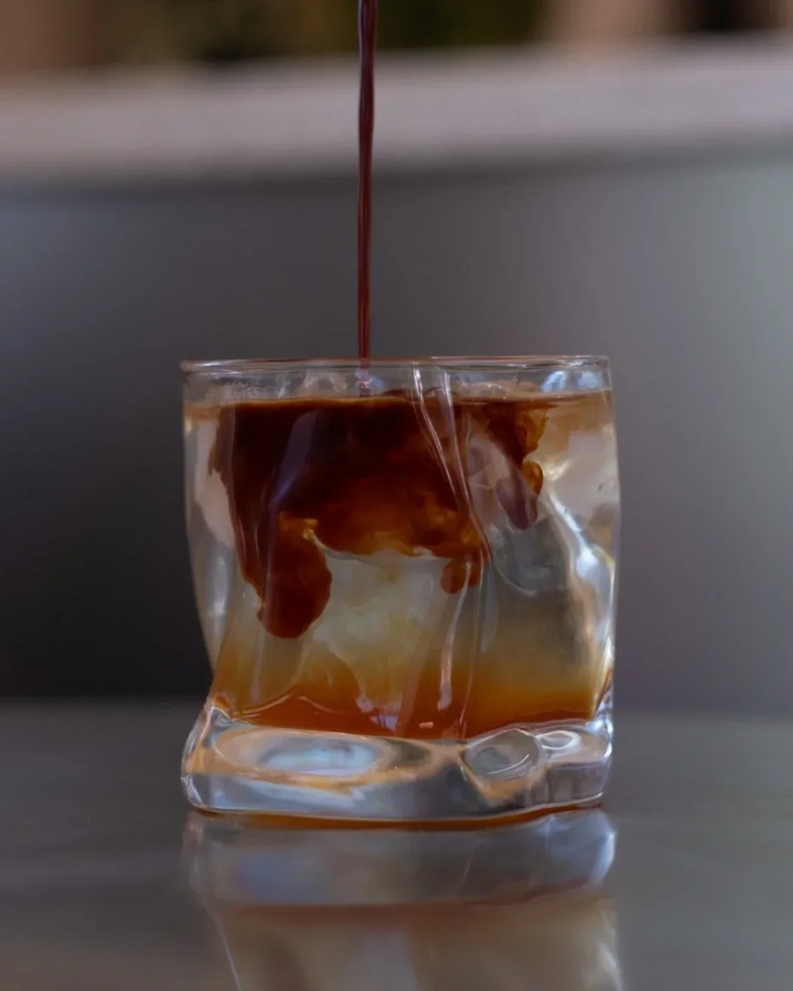 Ein Glas mit Eiswürfeln und dunkler Flüssigkeit wird mit Kaffee oder Tee gefüllt, der langsam ins Glas gegossen wird.