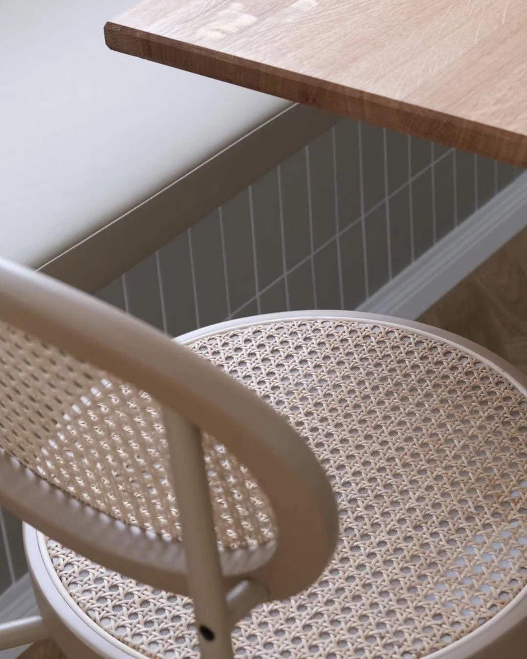 Ein runder Stuhl mit einem gestreiften, geflochtenen Sitz und einem Rückenlehnenrahmen aus Holz neben einem Tisch mit einer Holzplatte.