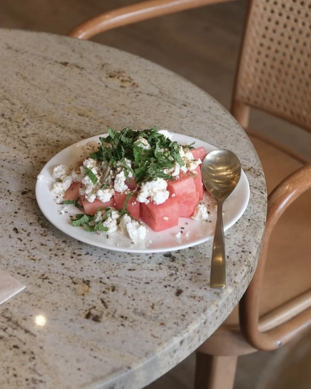 Ein Teller mit Wassermelonen, Feta-Käse und gehacktem Minz auf einem Tisch.