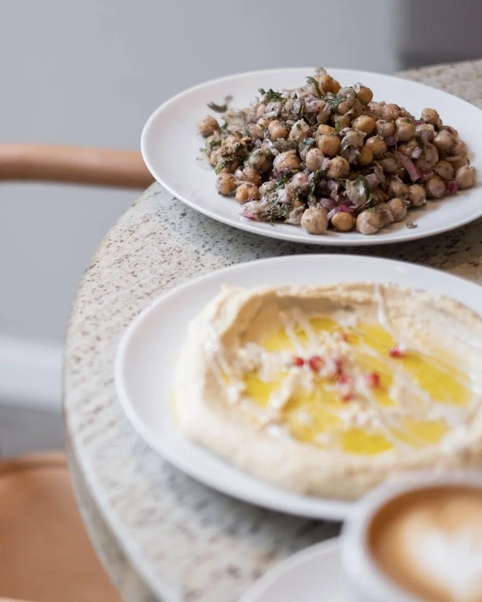 Verschiedene Gerichte auf weißen Tellern, darunter ein Kichererbsensalat und Fladenbrot mit Olivenöl, auf einem Marmor-Tisch.