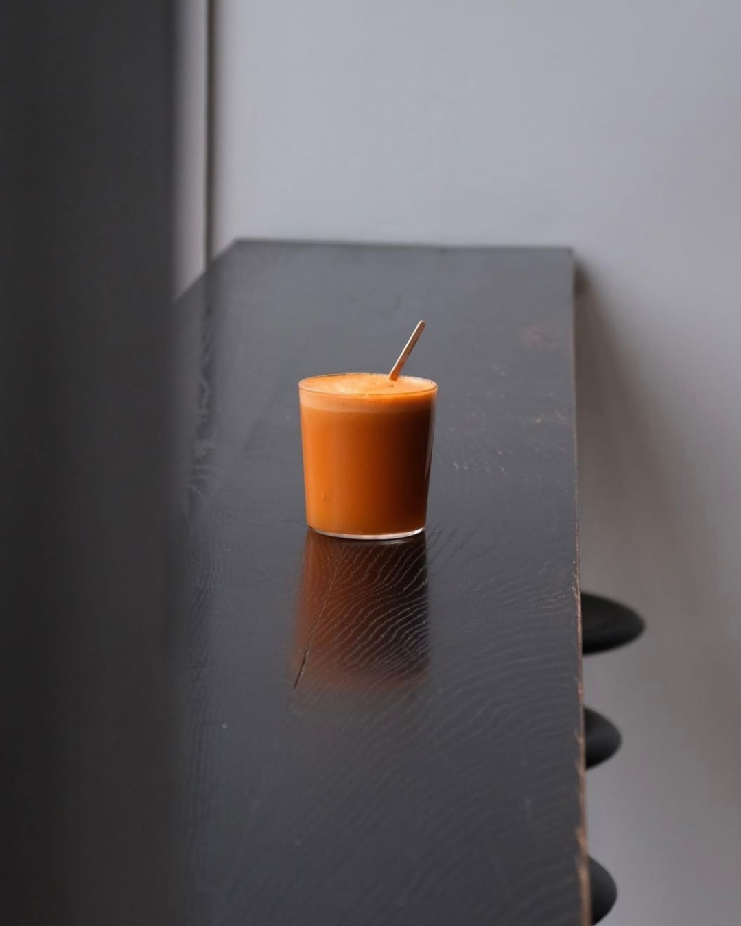 Ein Glas mit orangefarbiger Flüssigkeit auf einem dunklen Holztisch.