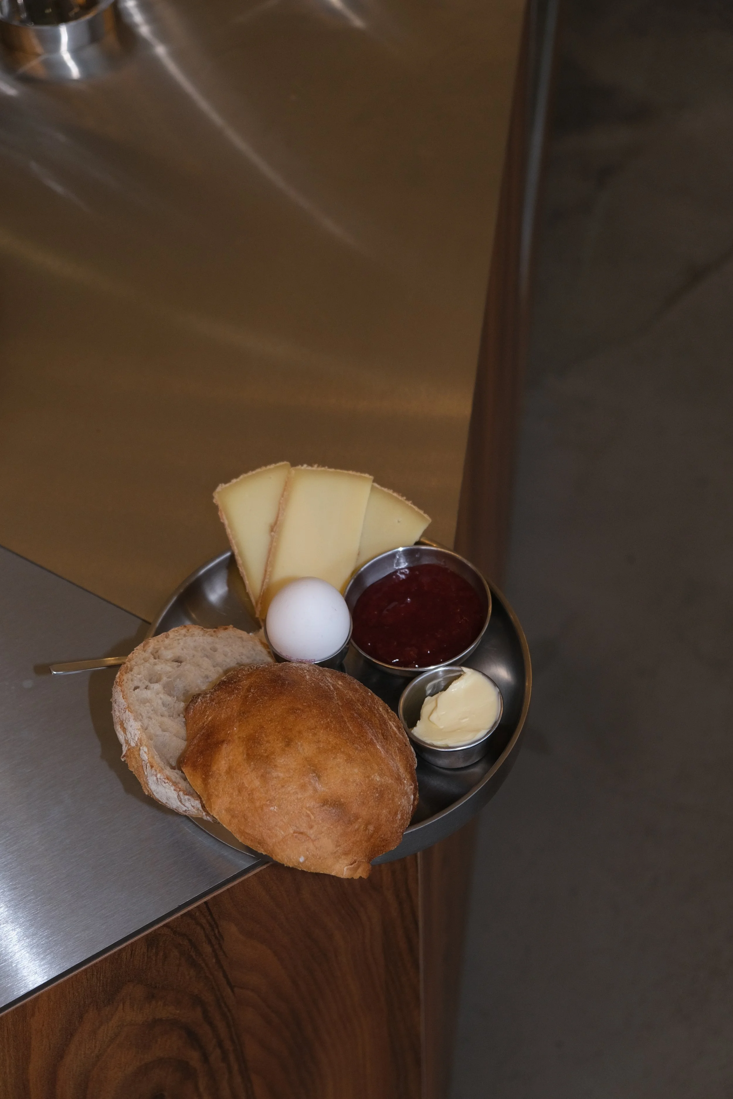 Ein Frühstücksteller mit Käse, hartgekochtem Ei, Brot, Brötchen, Butter, Marmelade und einem kleinen Löffel.