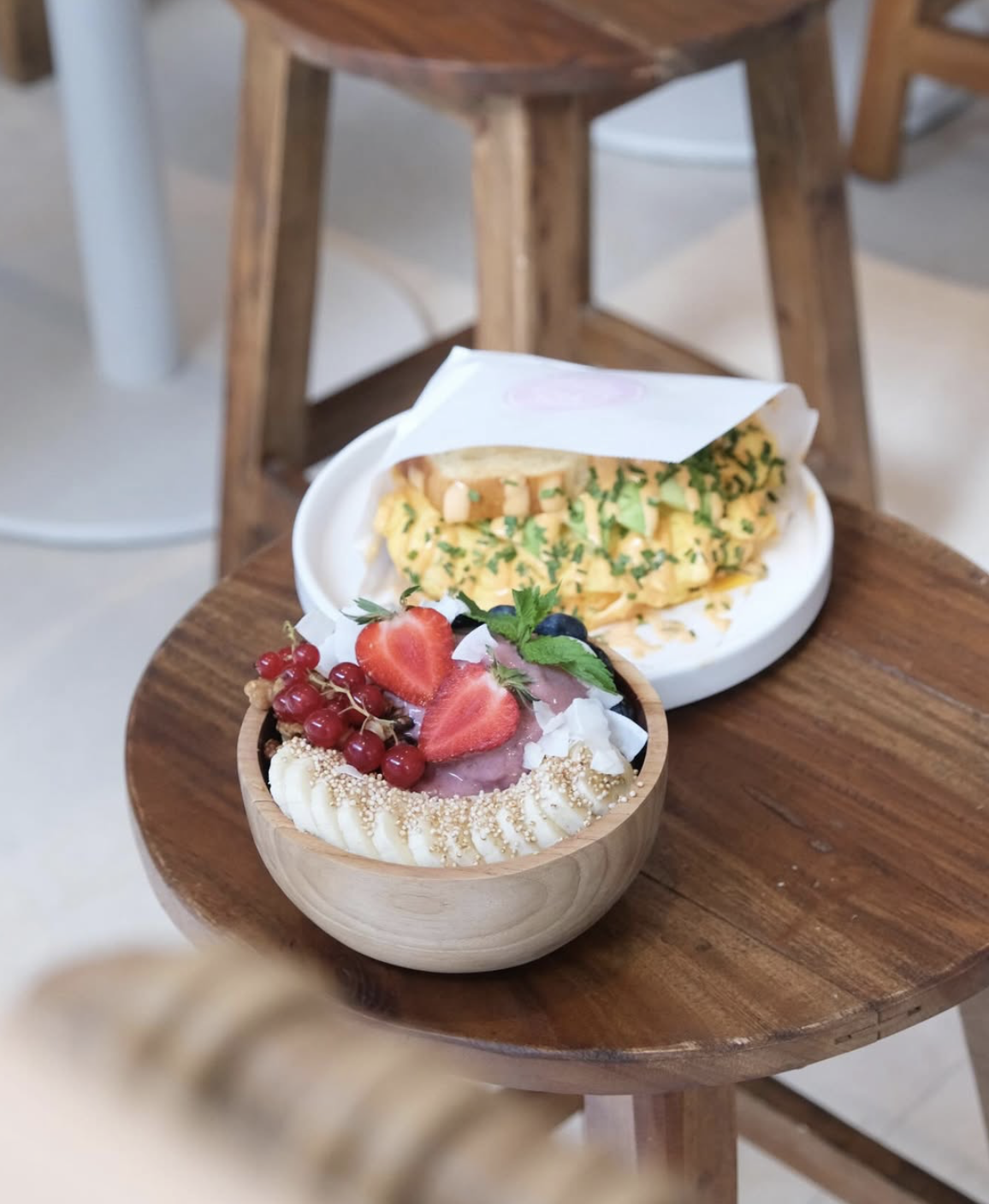 Ein Schüssel mit Himbeeren, Erdbeeren, roten Johannisbeeren und Kokosraspeln, und ein Teller mit einem Omelett, garniert mit Kräutern, auf einem kleinen Holz-Tisch.