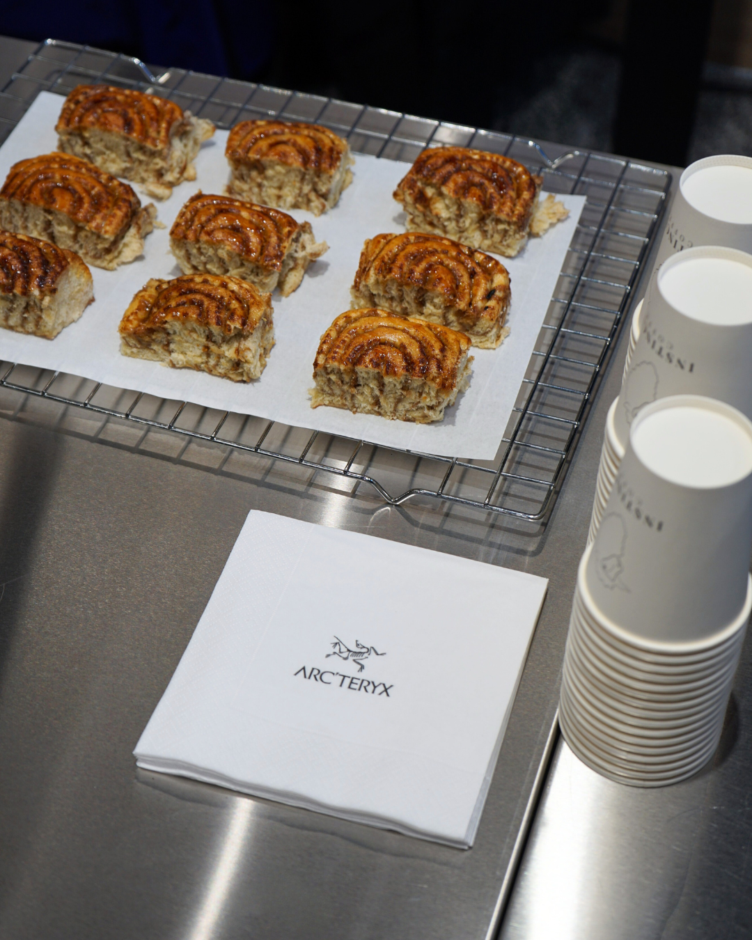 Frischer Zimtschnecken auf einem Backgitter mit Arc'teryx-Serviette und Pappbecher mit Milch oder Kaffee