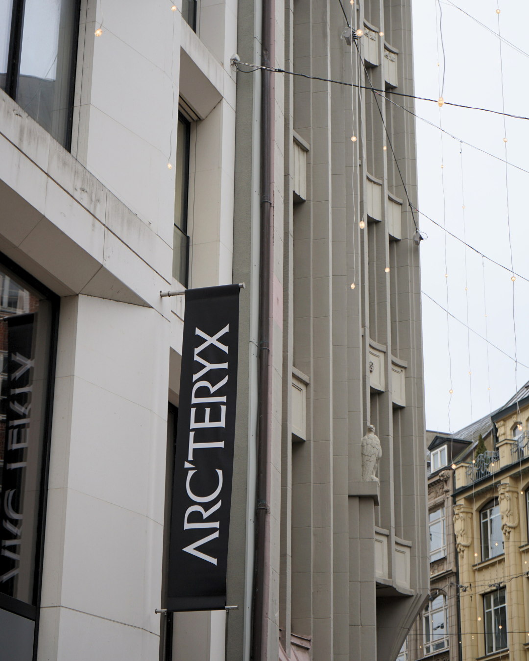 Außenansicht eines Gebäudes mit einem schwarzen, vertikalen Banner, auf dem 'ARCHETRYX' steht, sowie Kabel mit Lichterketten.
