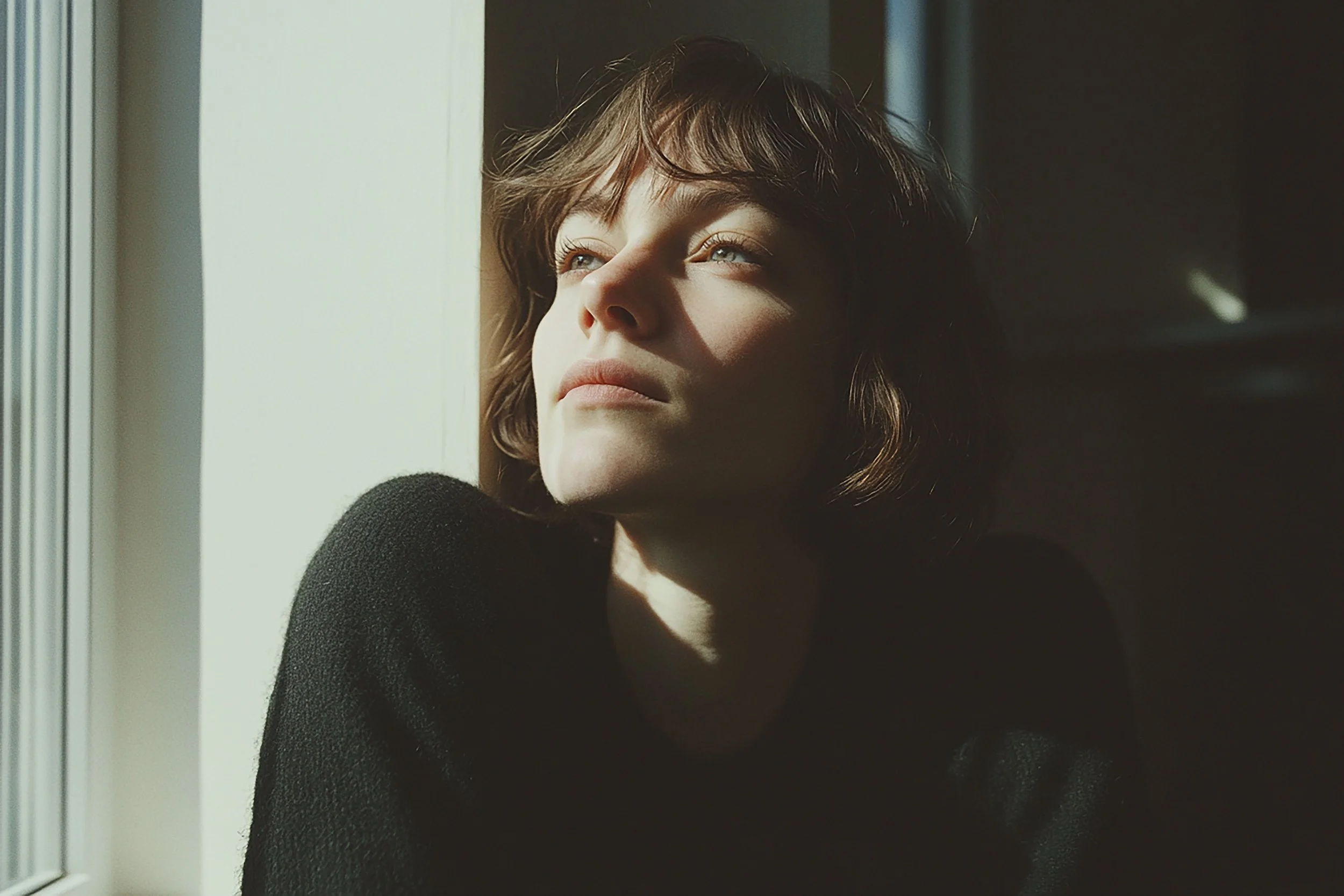 Woman lost in thought by window representing the inner journey of sacred feminine depth therapy