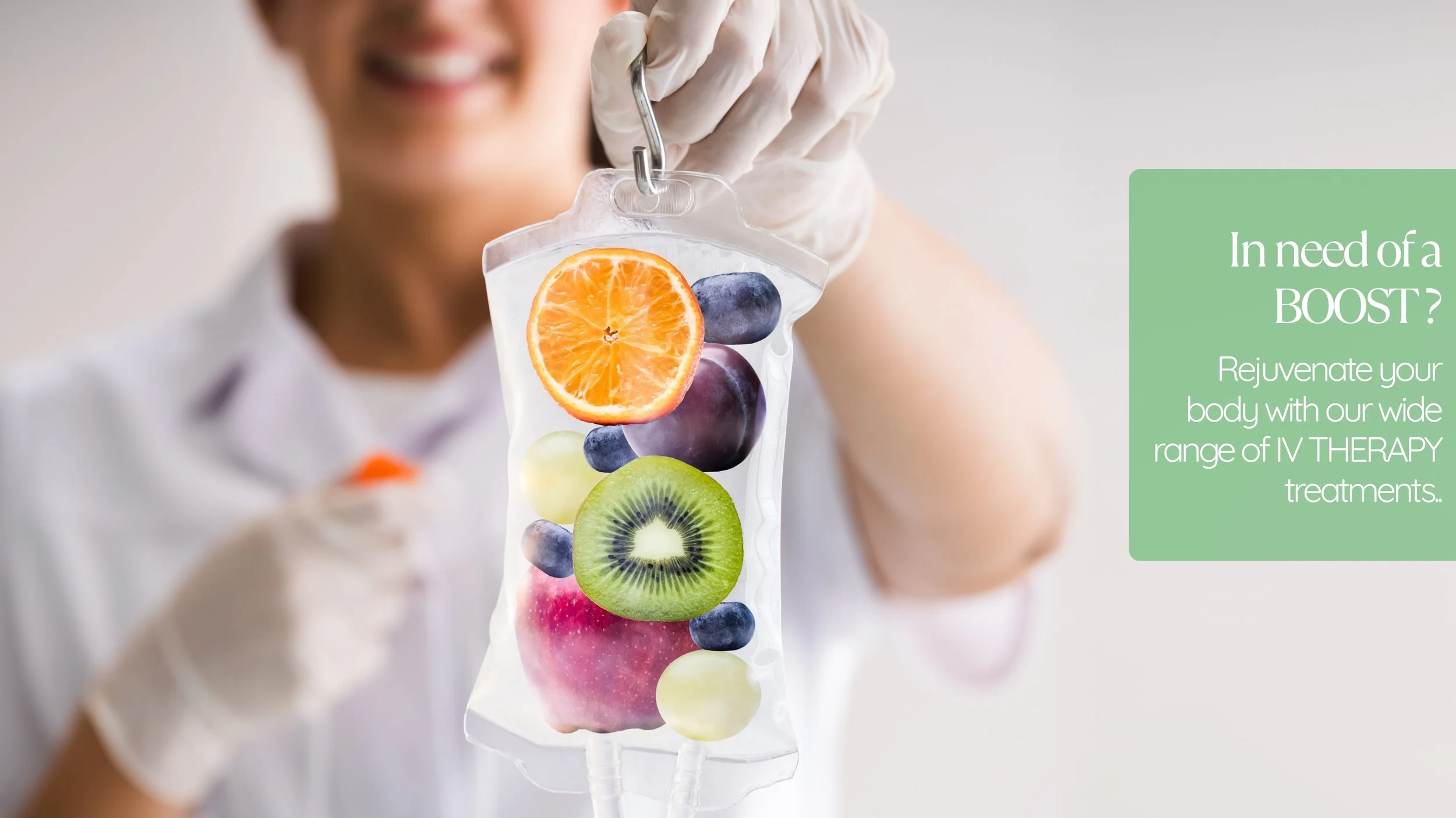 A smiling woman in a white medical coat and gloves holding a clear IV bag filled with floating fruit slices including orange, blueberry, apple, kiwi, and grape.