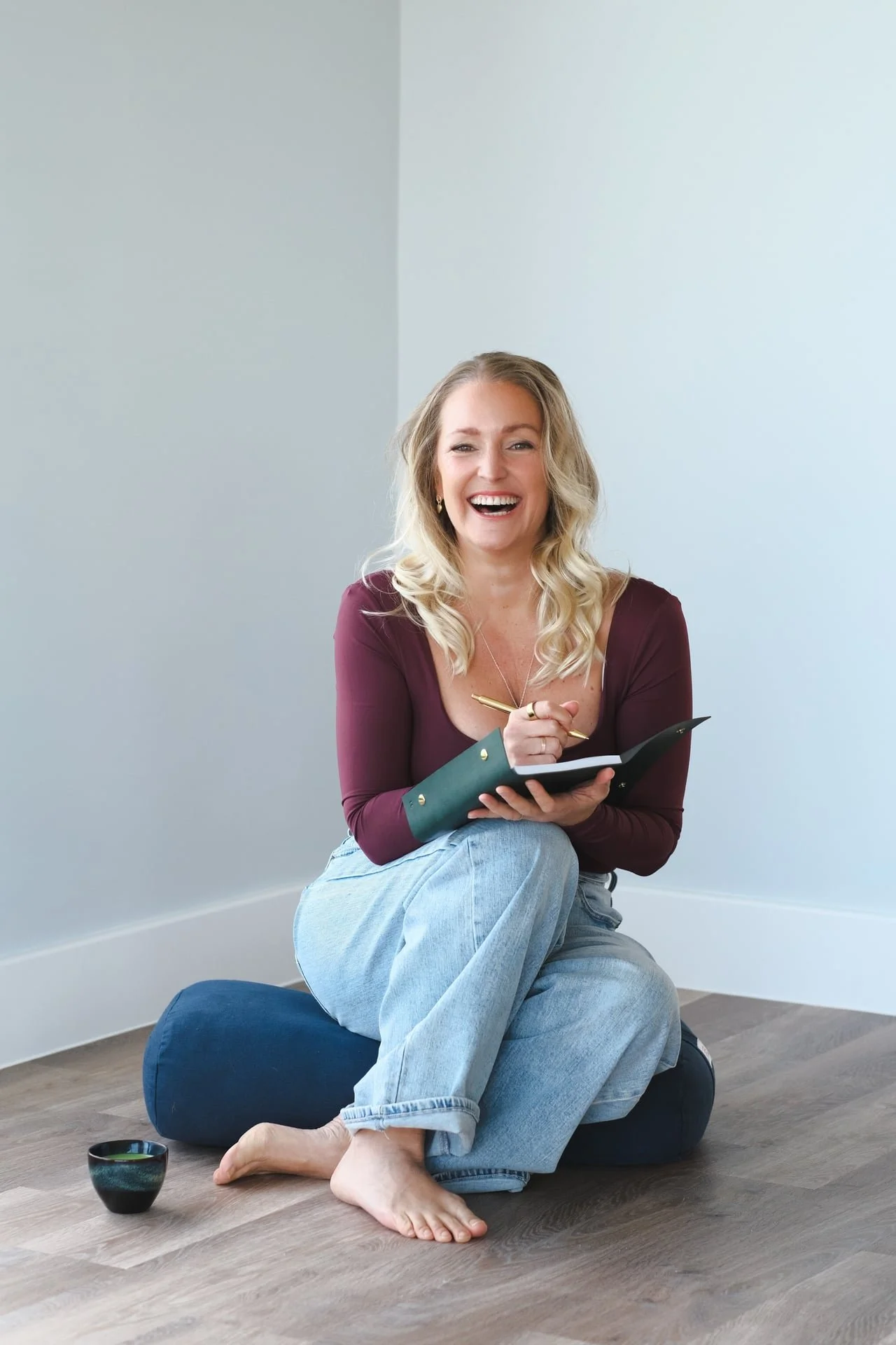 Woman sitting on a wooden floor journaling with notebook and pen, representing clarity, reflection and somatic integration for nervous system and personal growth work