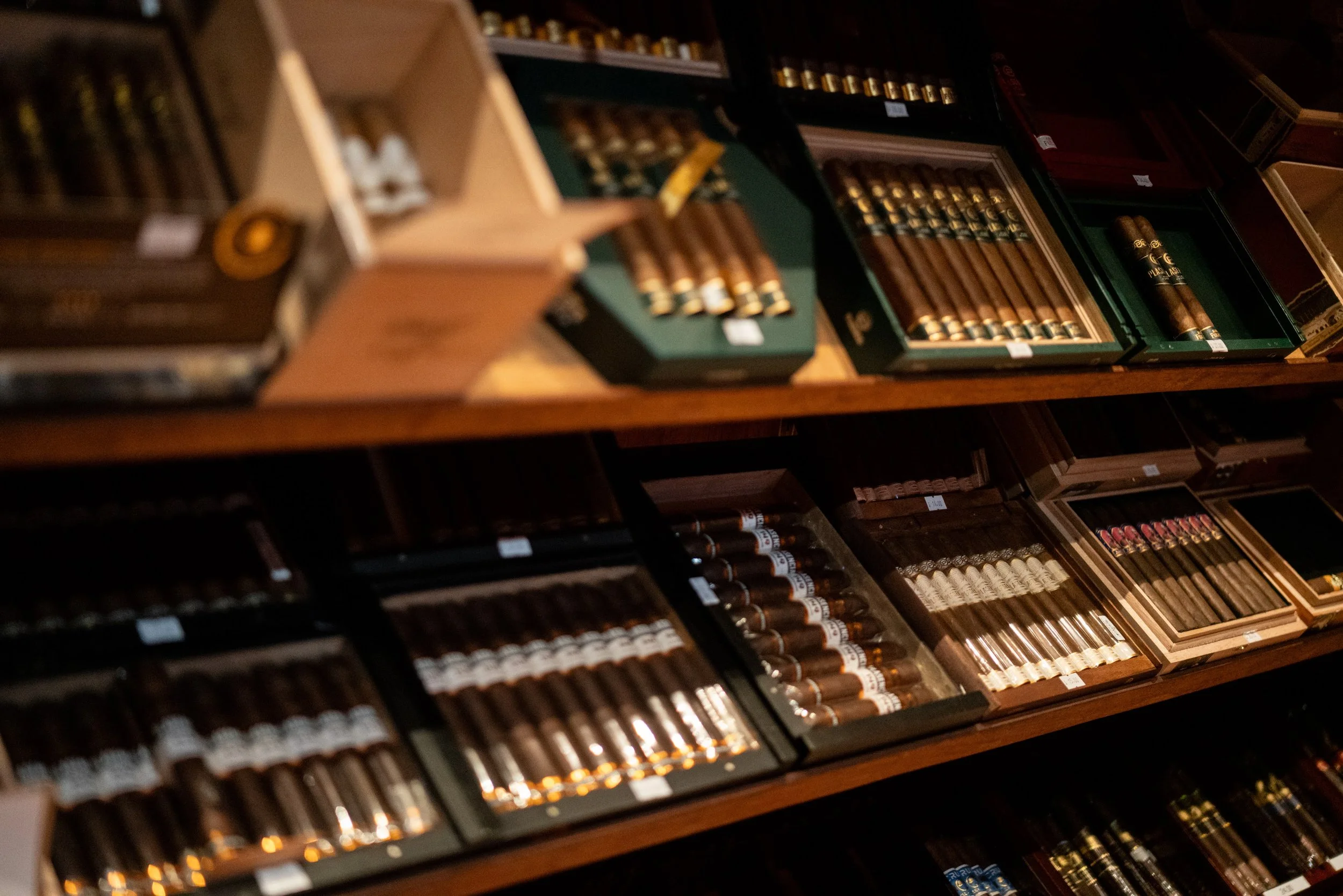 Display of various cigars in boxes on wooden shelves.